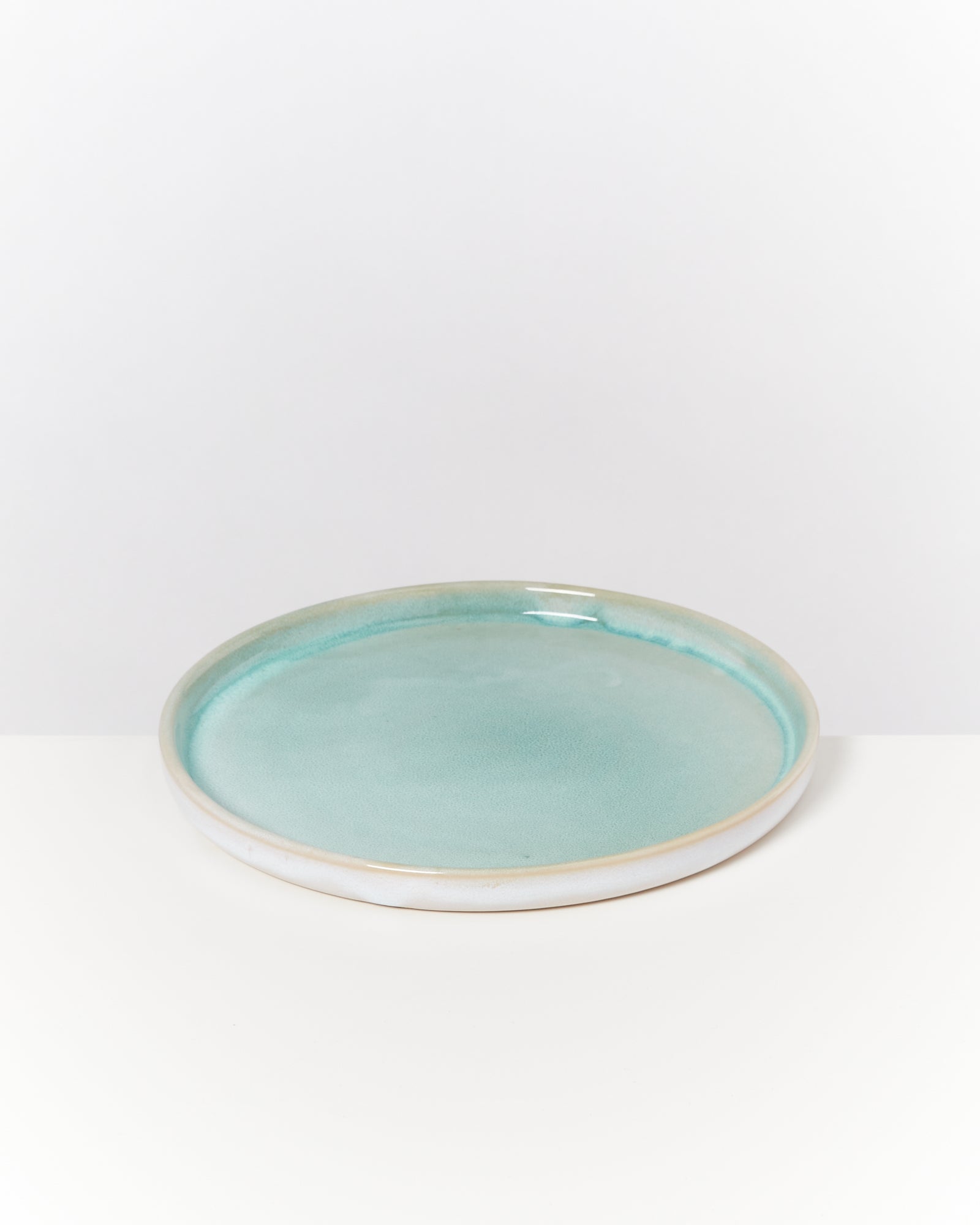 Ein flacher, runder Keramikteller mit einem blauen, glänzenden Finish, auf einem weißen Hintergrund.