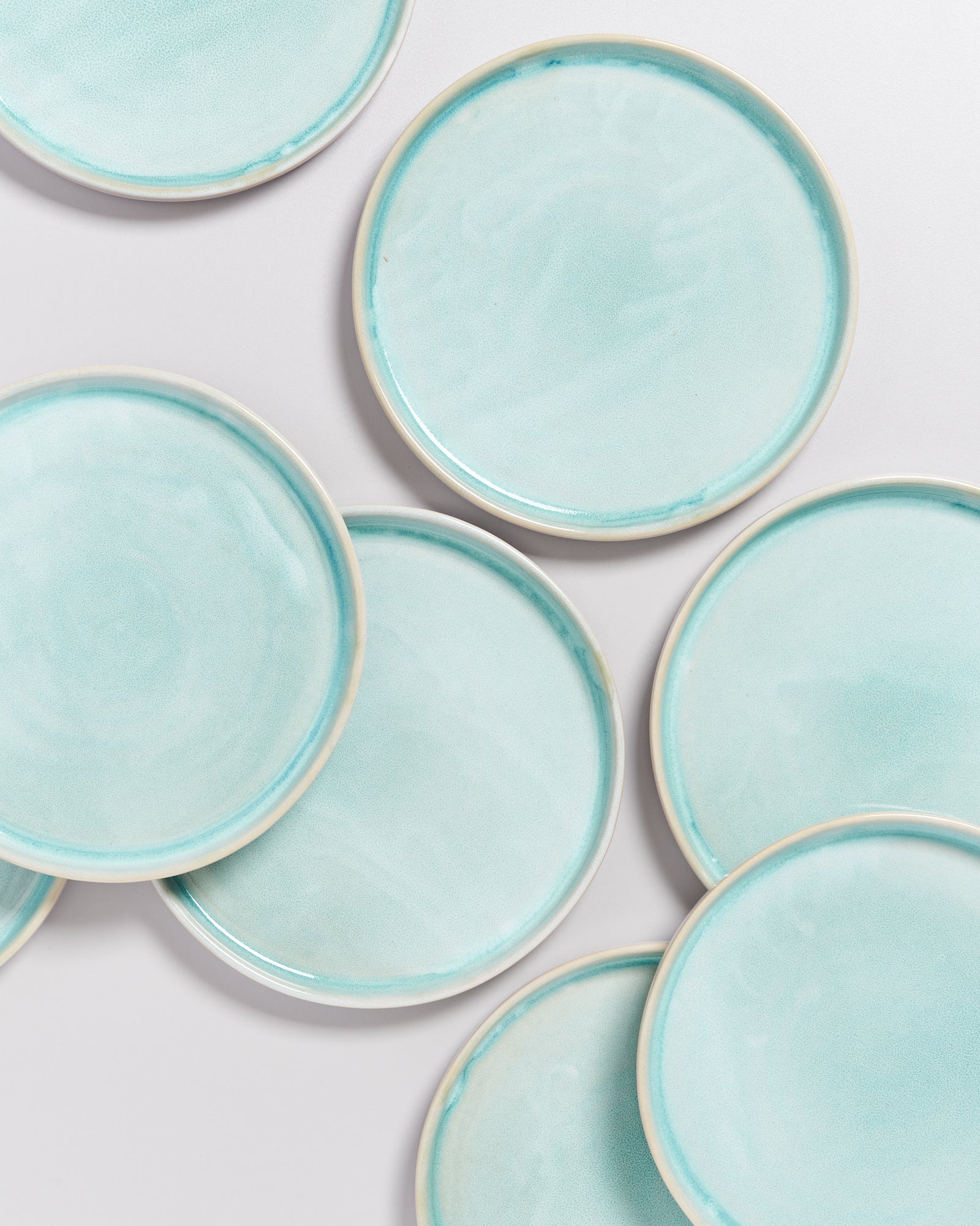 Mehrere hellblaue, runde Keramikteller liegen auf einer weißen Oberfläche.