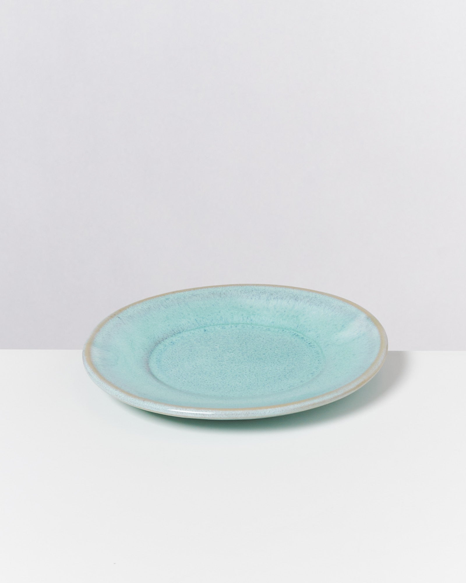 Ein türkisfarbener flacher Teller mit natürlicher Textur liegt auf einer weißen Oberfläche.
