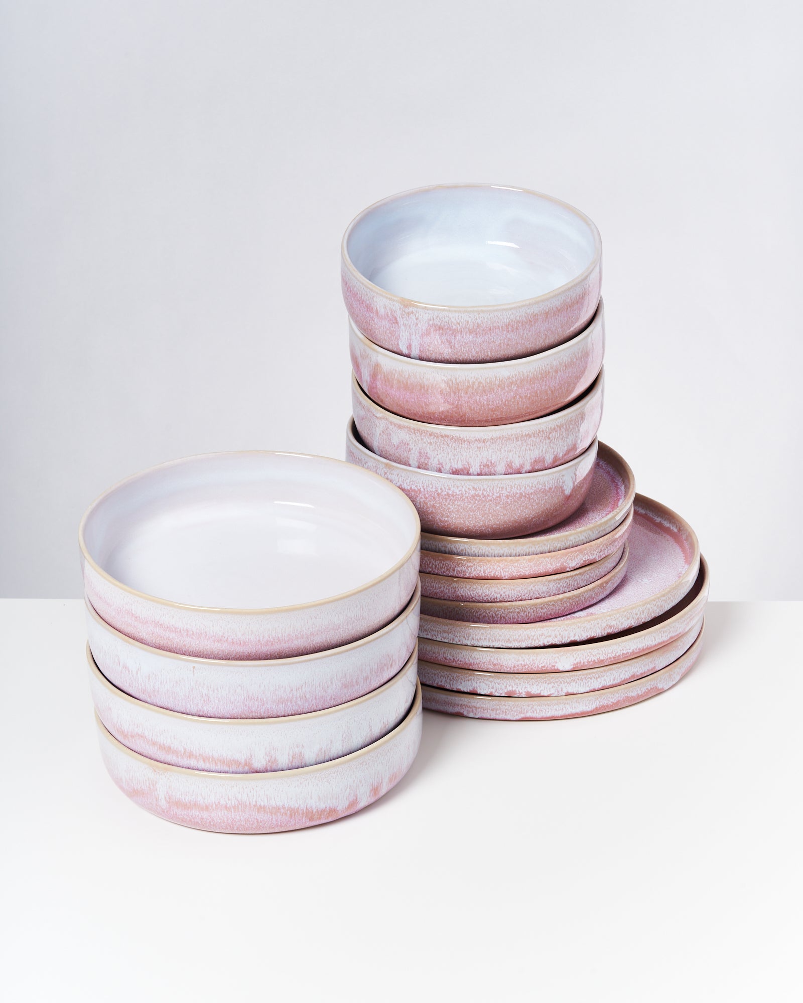 Stapel von flachen und tiefen rosafarbenen Tellern auf einem weißen Tisch.