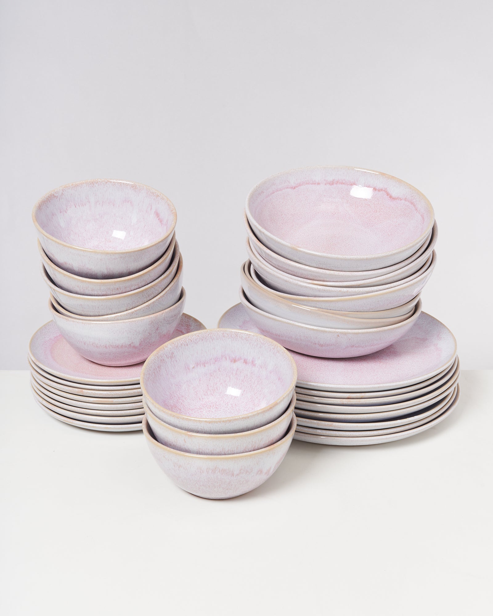 Stapel rosa und lila Keramikschalen und -teller auf einem weißen Untergrund.