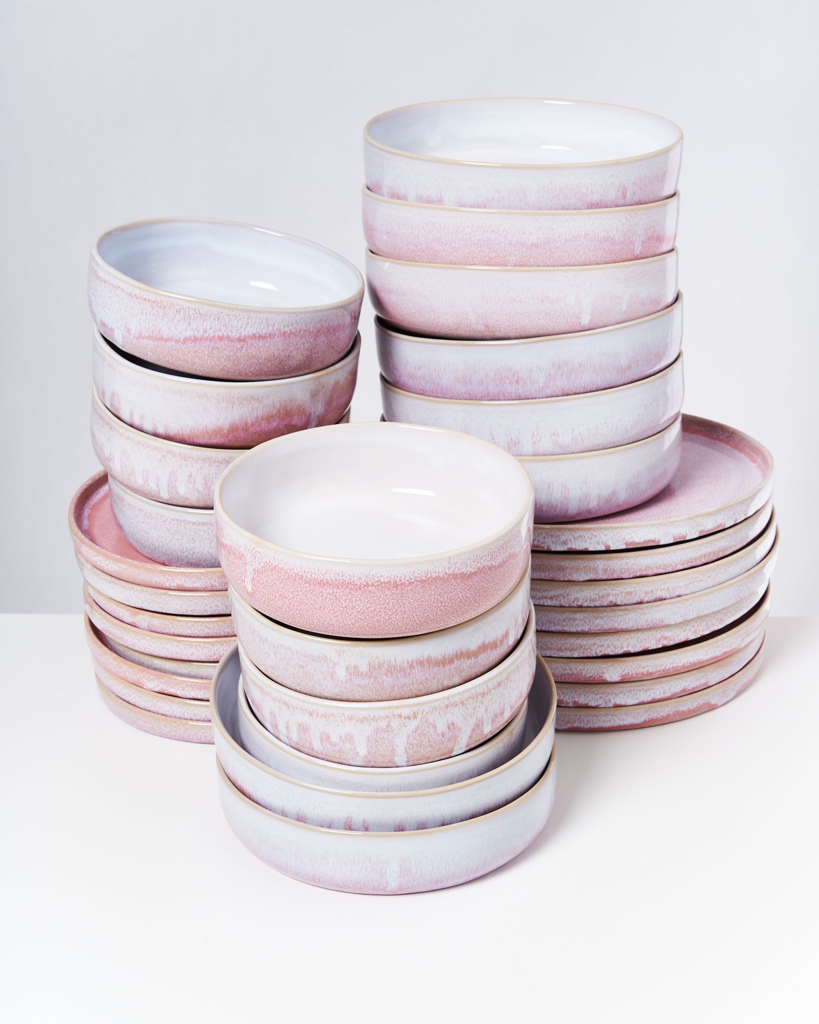 Gestapelte Teller und Schüsseln aus Keramik mit rosa und weißen Tönen auf weißem Hintergrund.