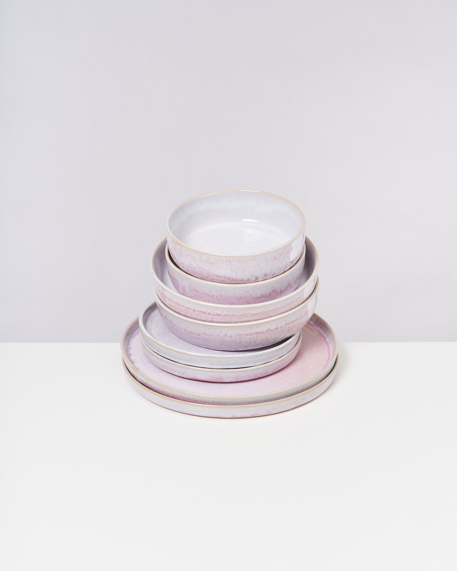 Ein Stapel aus vier rosafarbenen und weißen Keramiktellern und Schüsseln auf einem weißen Hintergrund.