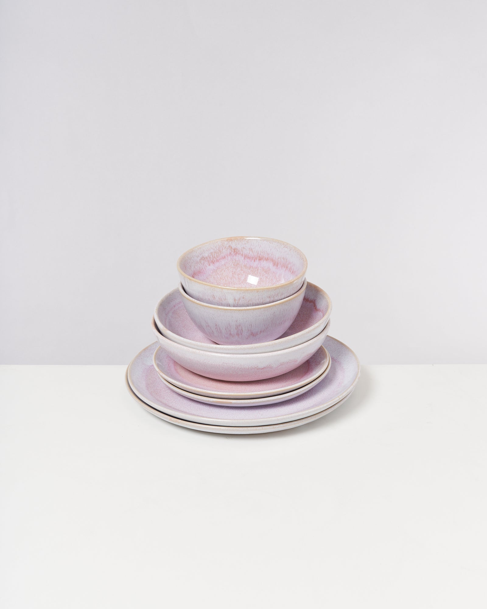 Ein Stapel von vier rosafarbenen Keramikschalen und Tellern auf einem weißen Hintergrund.