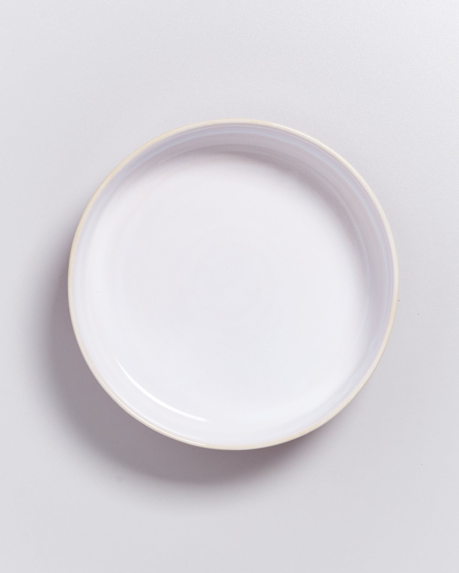 Ein weißer, runder Keramikteller auf einem hellen Untergrund.