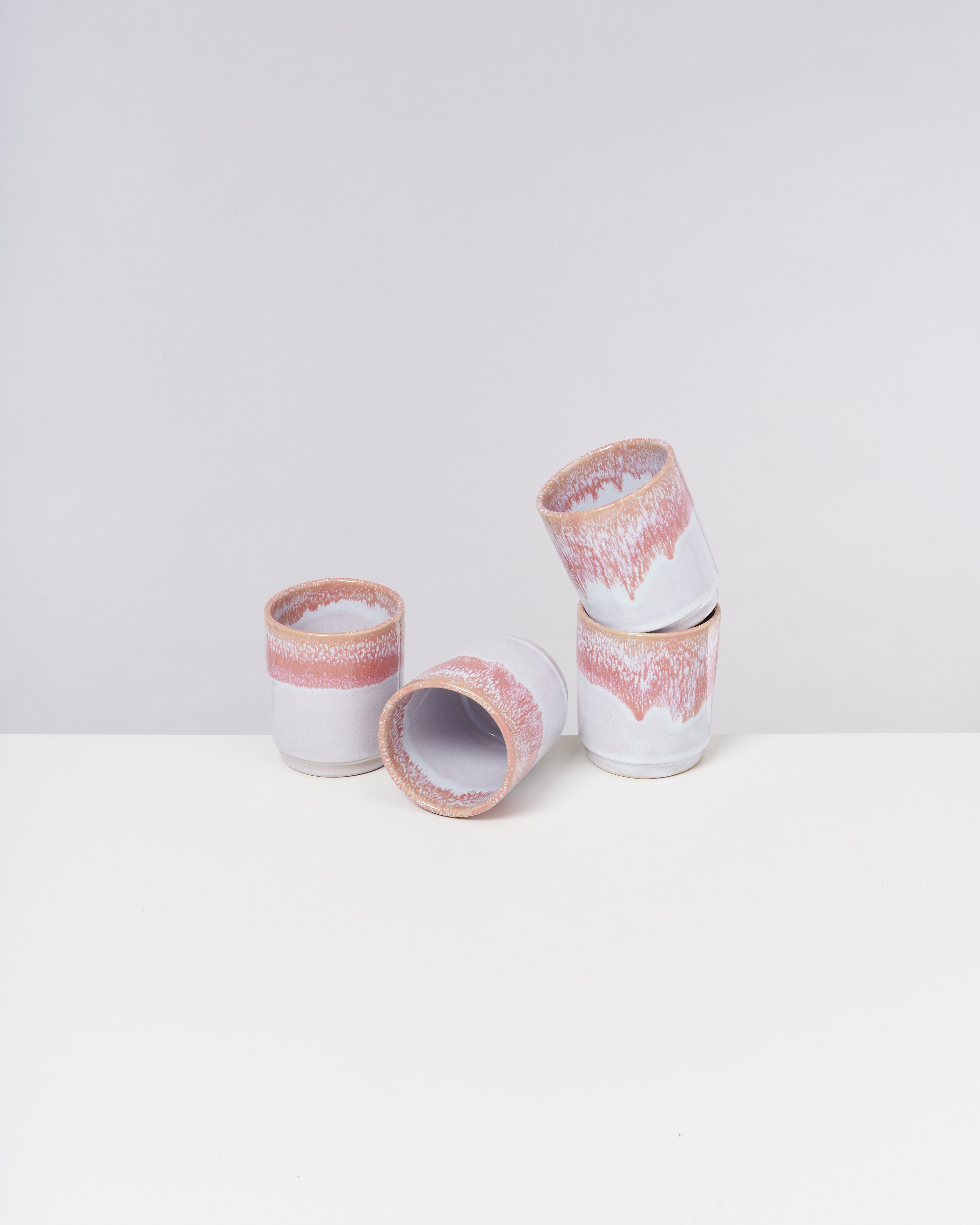 Drei weiße Tassen mit rosa Mustern stehen auf einem weißen Tisch, eine davon liegt seitlich.