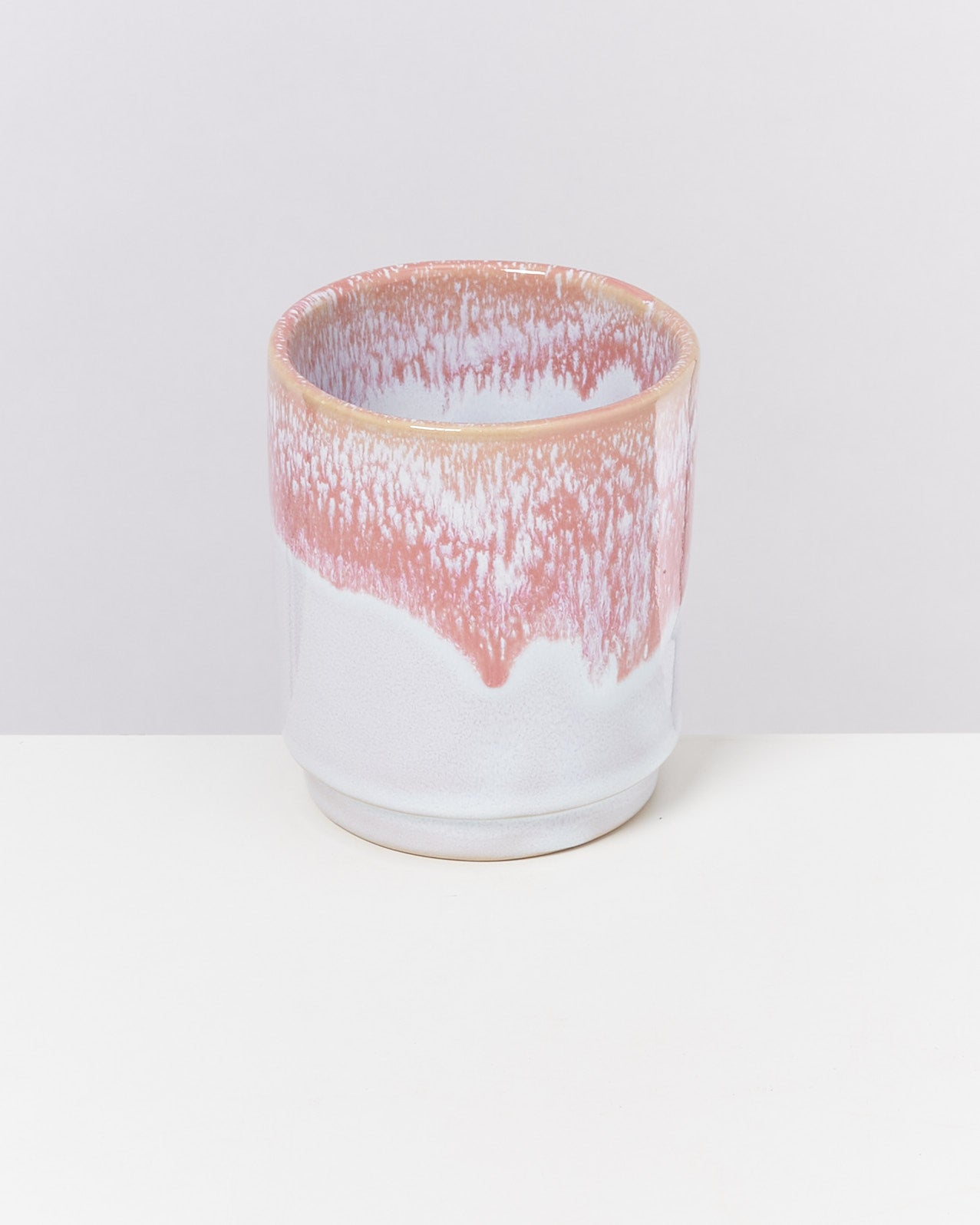 Keramiktasse mit rosa-weißem Muster auf weißem Hintergrund.