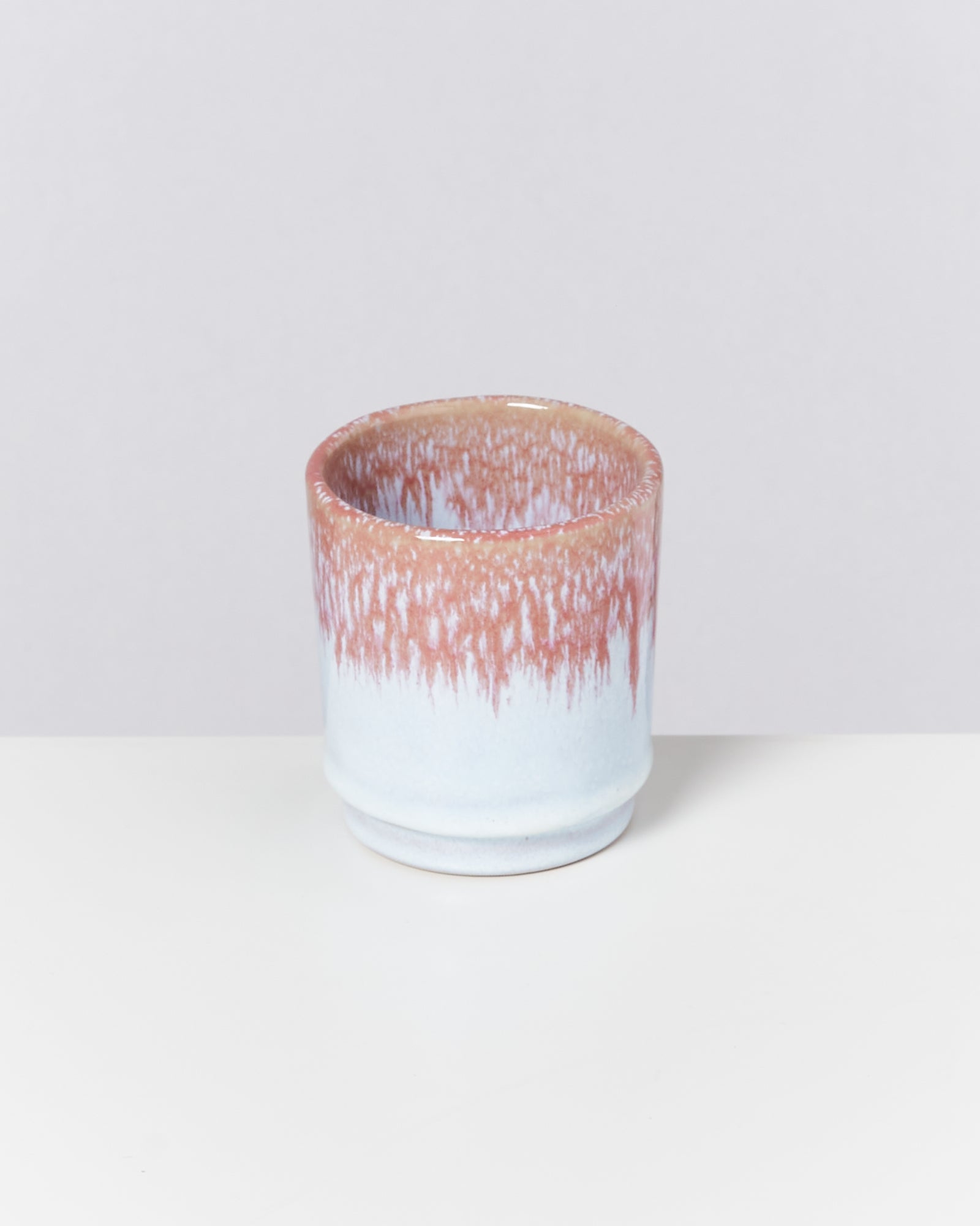 Keramikbecher mit rötlich-weißer Glasur auf weißem Hintergrund.