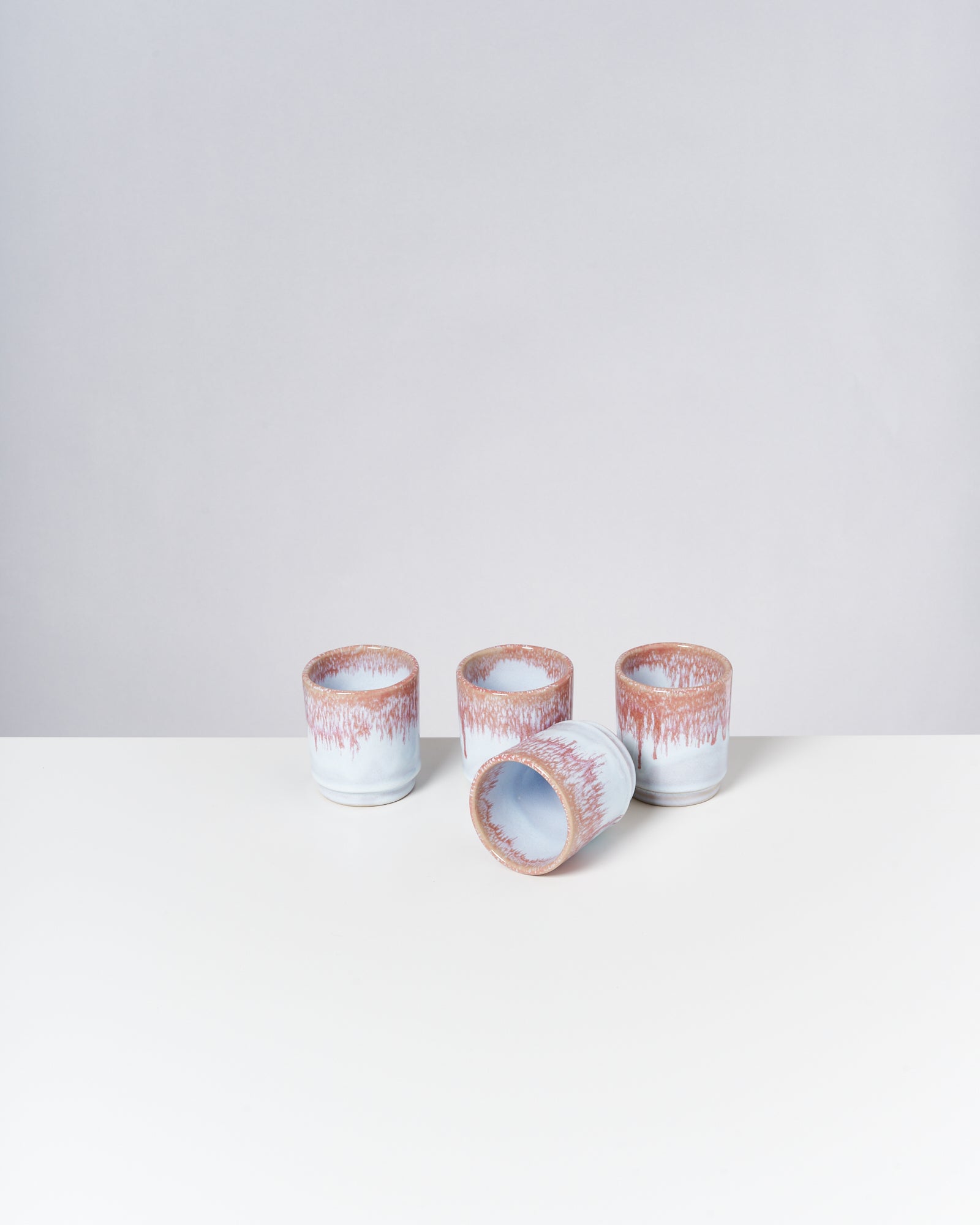 Vier weiße Becher mit braunen Details stehen auf einem weißen Tisch, einen Becher liegend.