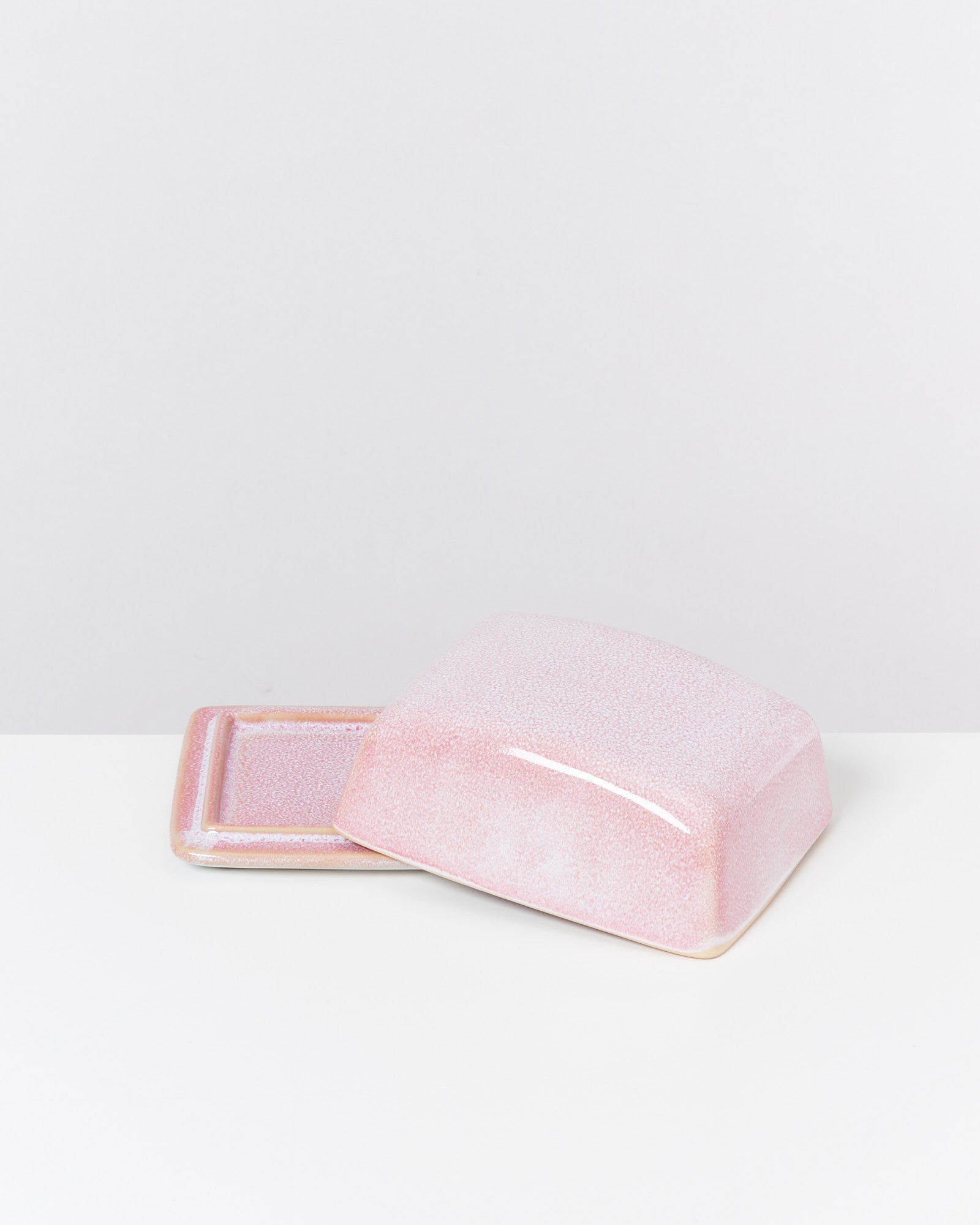 Rosa Butterdose aus Keramik mit abgenommenem Deckel auf weißem Hintergrund.