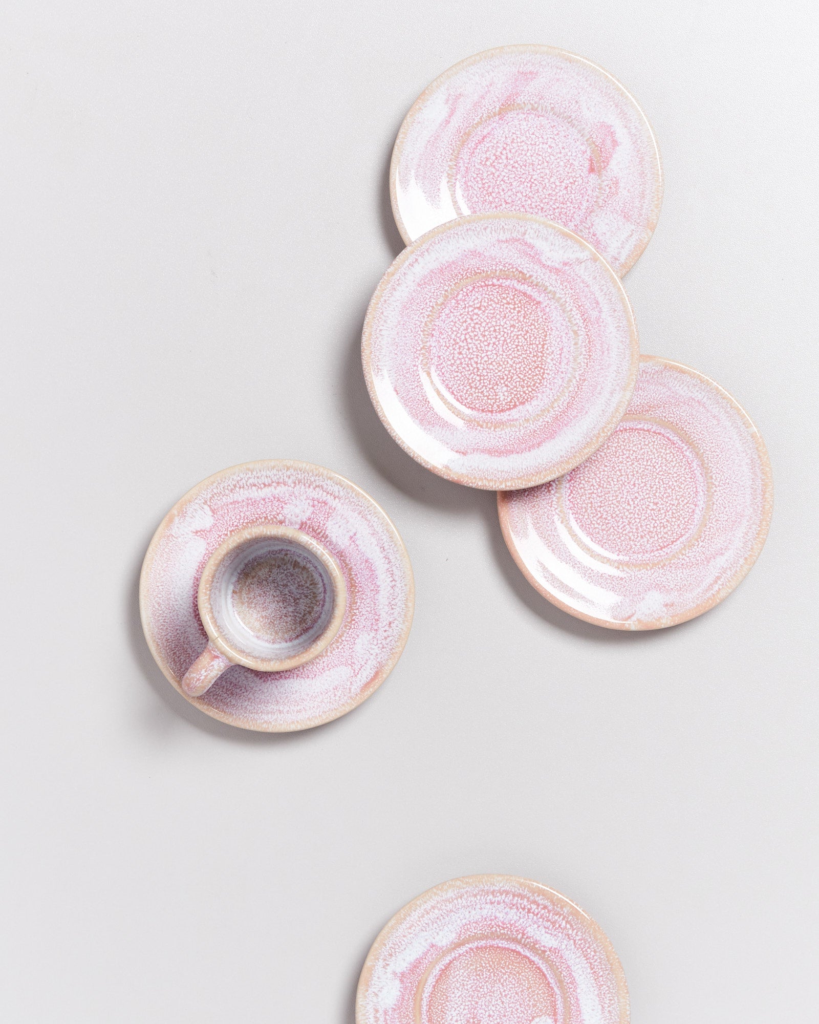 Sechs pastellfarbene Untertassen und eine kleine Tasse aus Keramik auf weißem Hintergrund angeordnet.