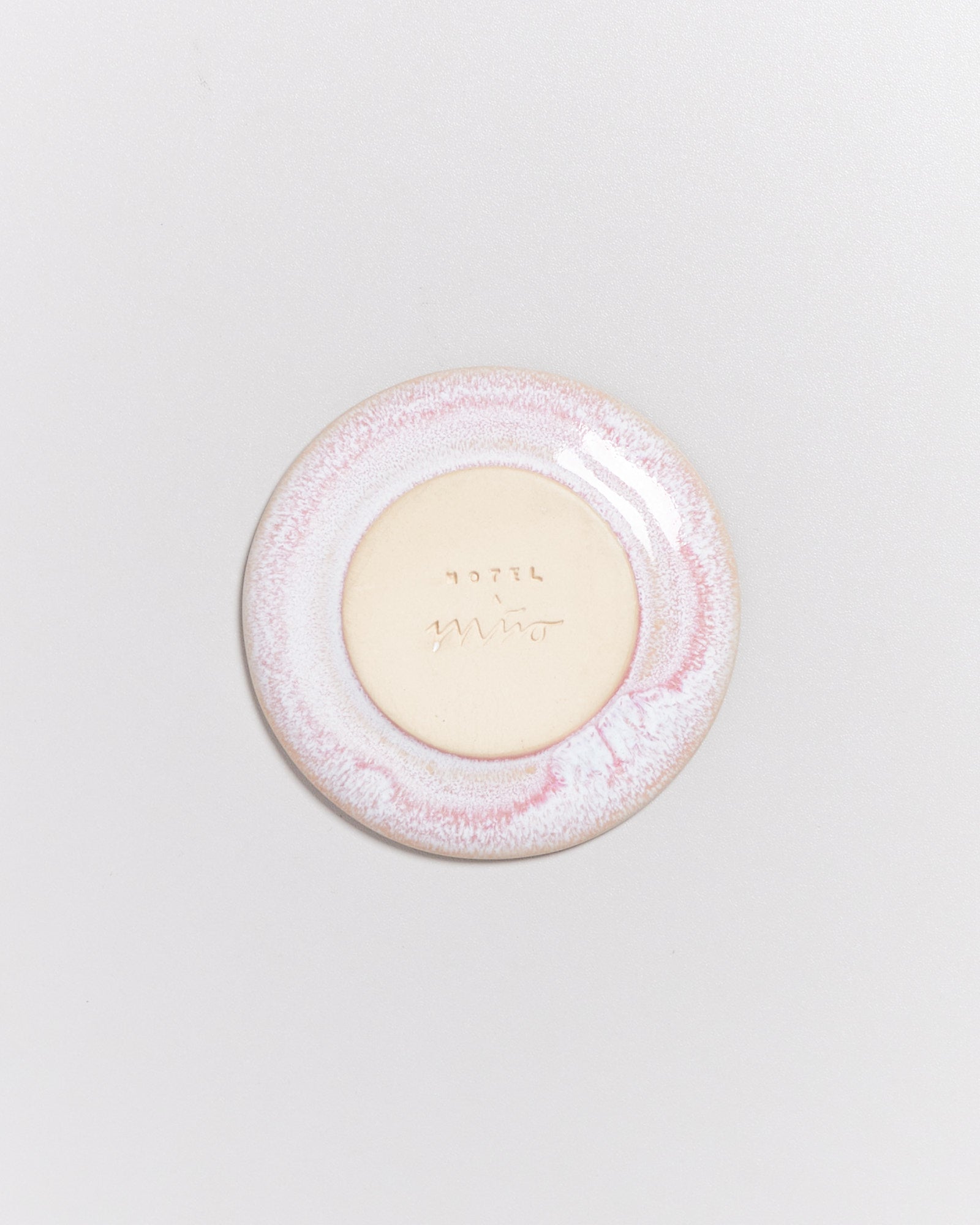 Eine kleine, runde Keramikunterseite mit heller Mitte und rosa Rand auf hellem Hintergrund.