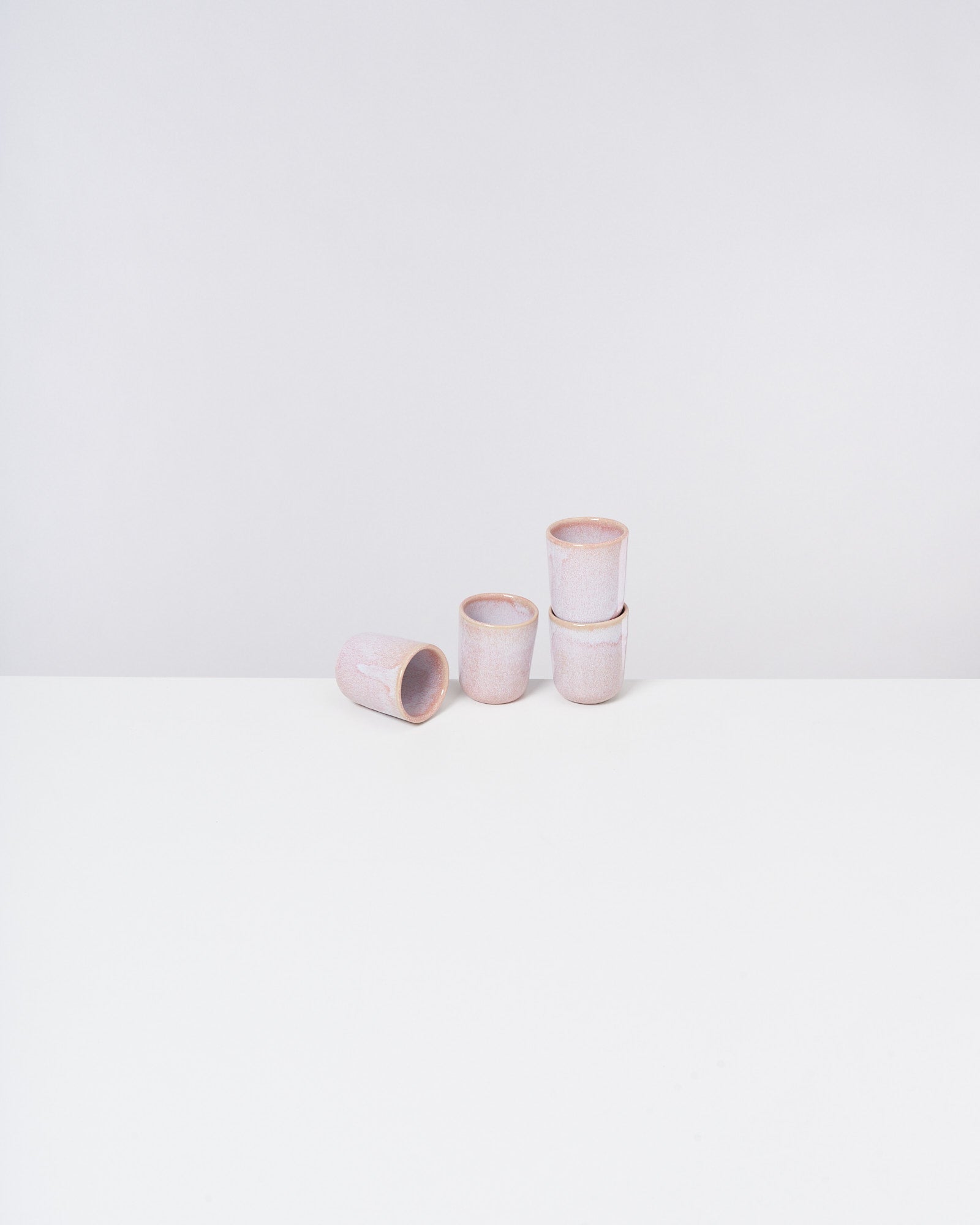 Vier rosafarbene Keramikbecher stehen auf einem weißen Tisch, einer liegt seitlich.