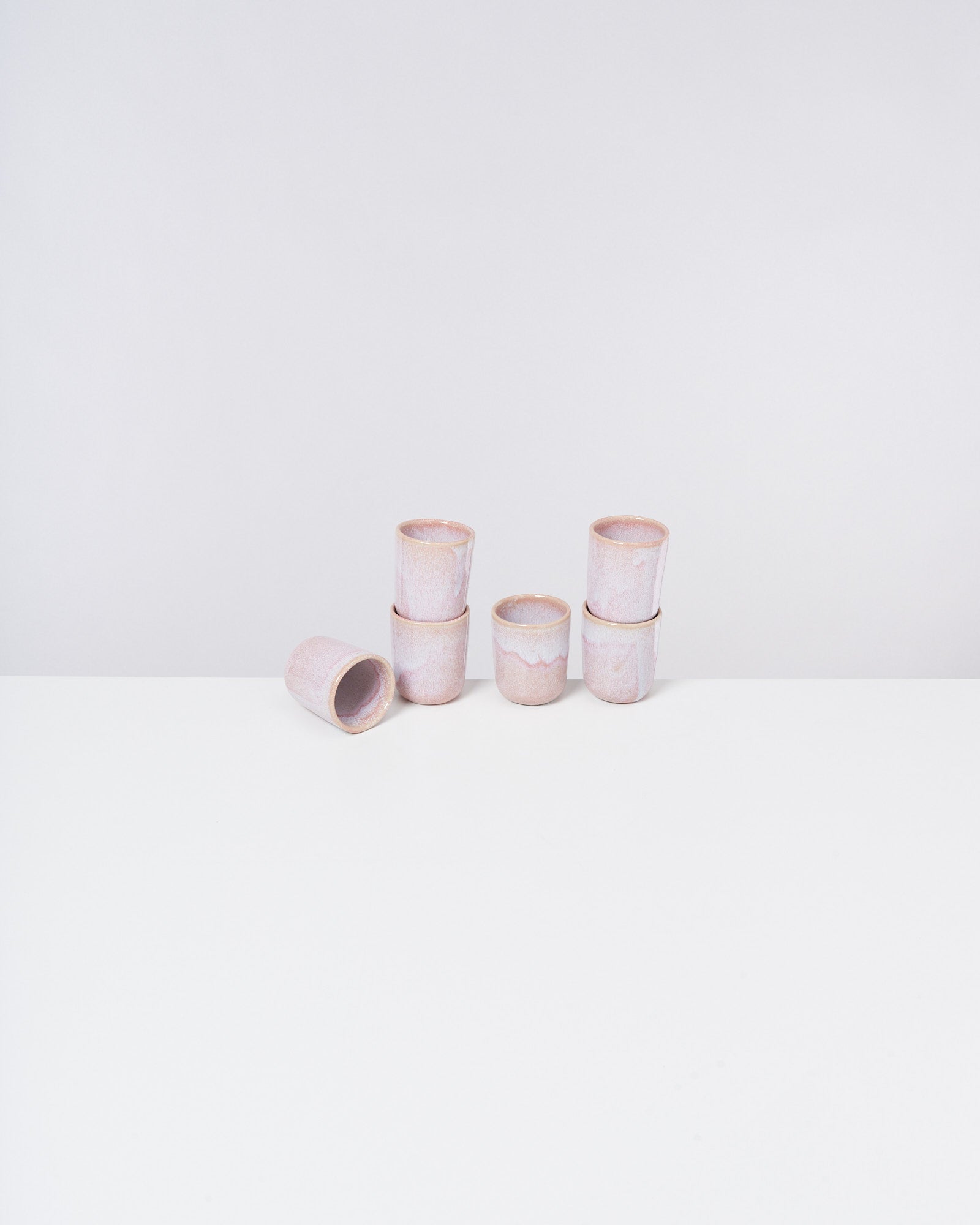 Sieben rosa Keramiktassen auf einem weißen Tisch, eine liegt seitlich.
