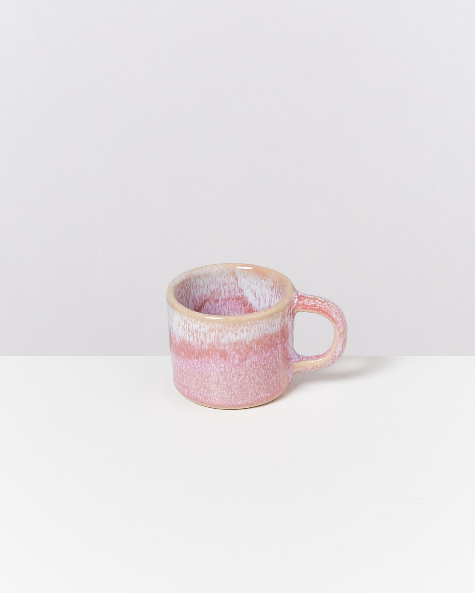 Rosa Keramiktasse mit weißem und beigem Verlauf, auf einem weißen Tisch vor grauem Hintergrund.
