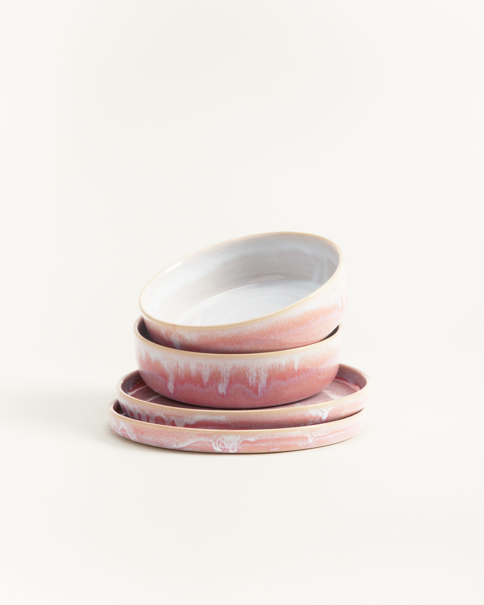 Ein Stapel von vier rosa-weißen, handgefertigten Keramiktellern vor einem weißen Hintergrund.