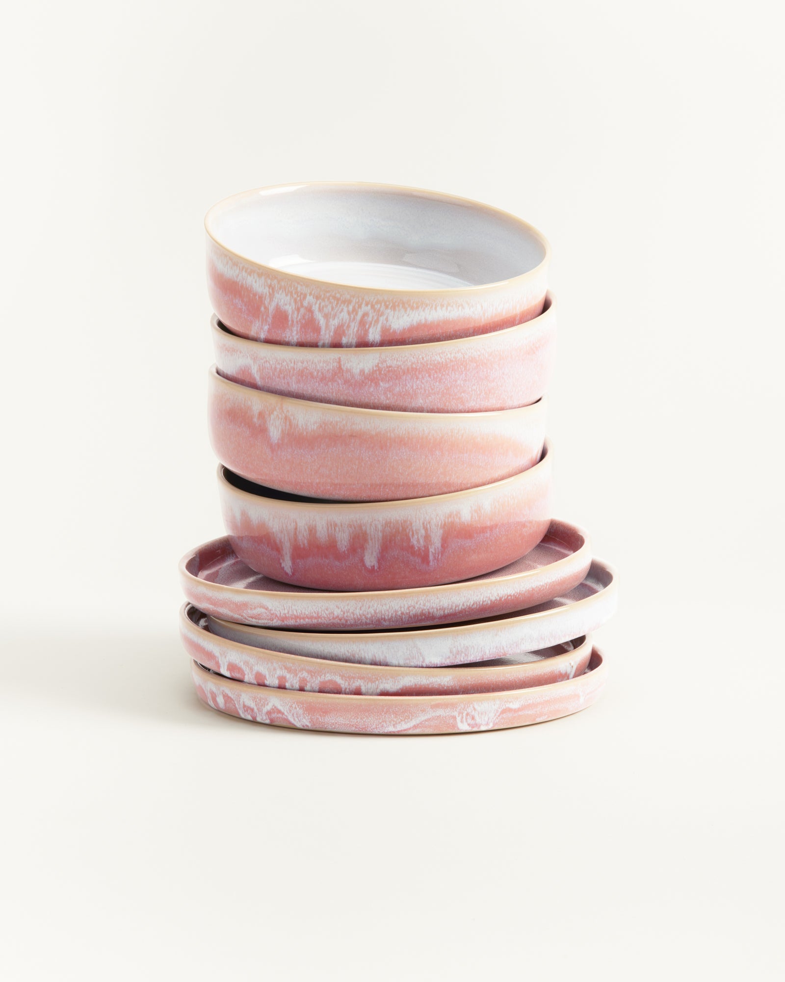 Ein Stapel von rosa-weißen Keramiktellern und -schüsseln auf weißem Hintergrund.