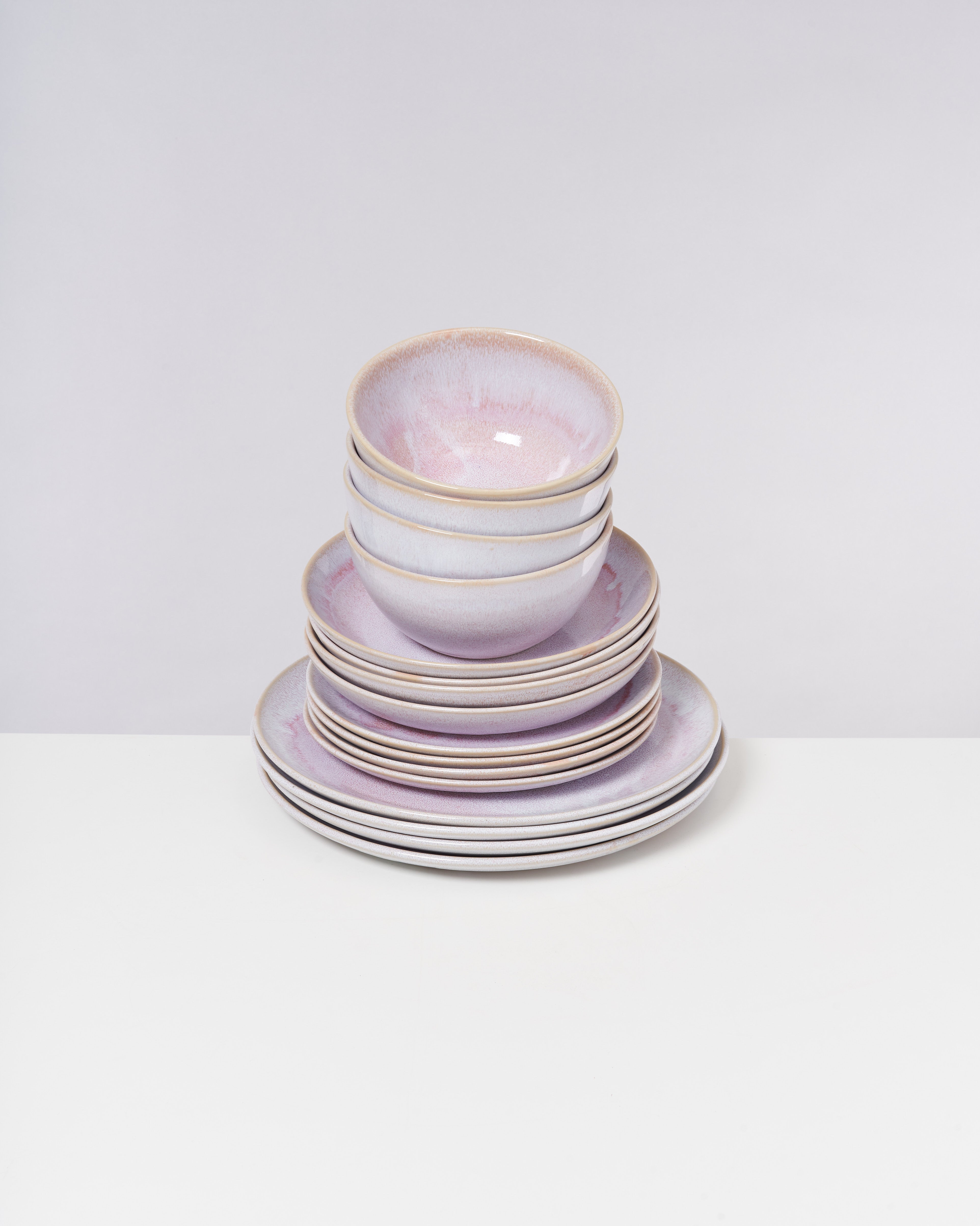 Ein Stapel keramischer Schalen und Teller in pastelligen Farben steht auf einem weißen Tisch vor einer grauen Wand.
