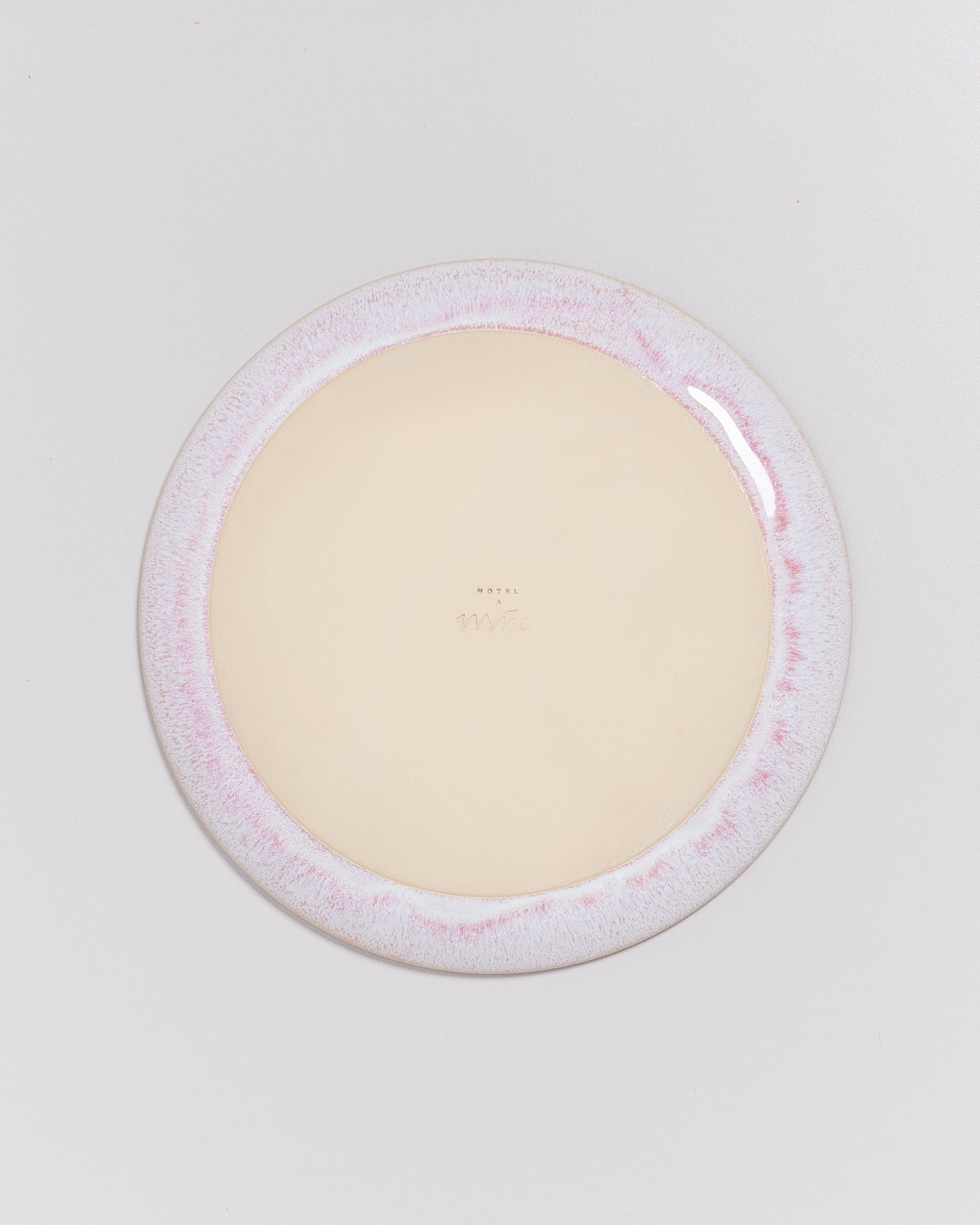 Runder Teller mit einem hellen, rosa gesprenkelten Rand, auf einem hellgrauen Hintergrund liegend.