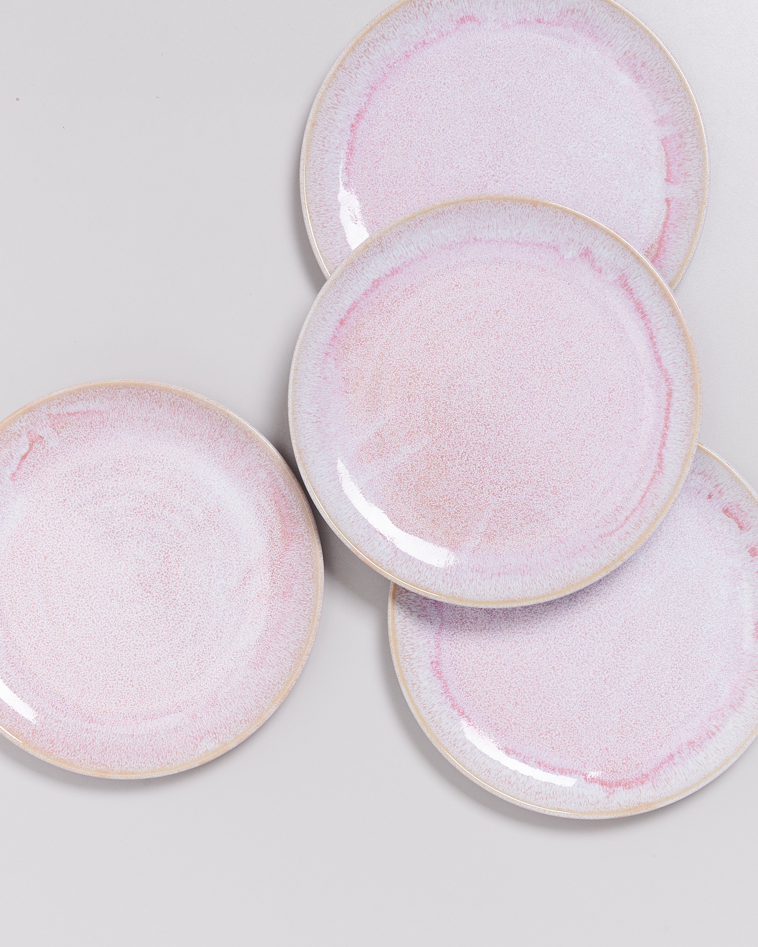 Vier rosafarbene Teller mit dezentem Muster liegen auf einer hellgrauen Oberfläche.