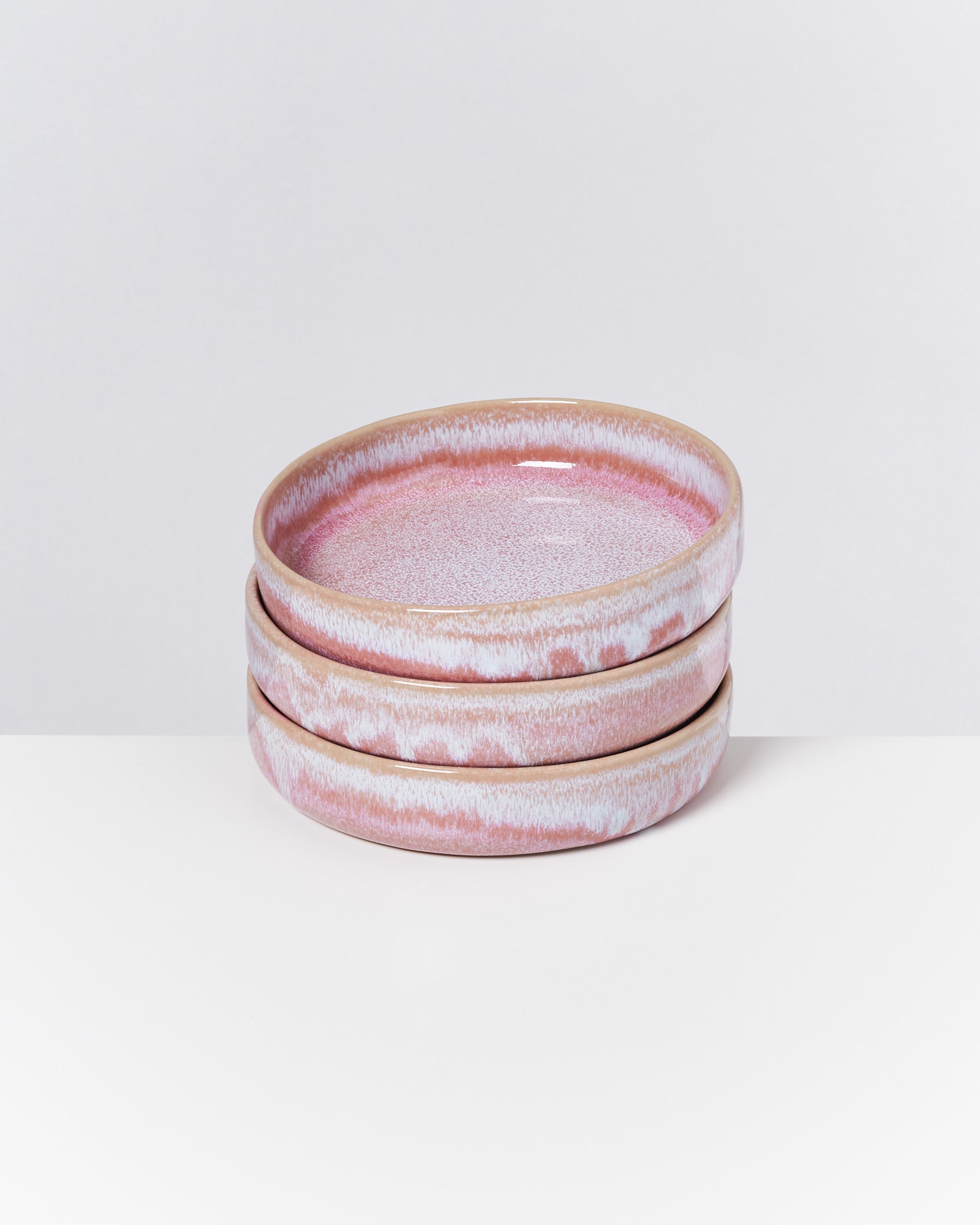 Drei gestapelte, rosa-weiß glasierte Keramikteller auf einem weißen Hintergrund.
