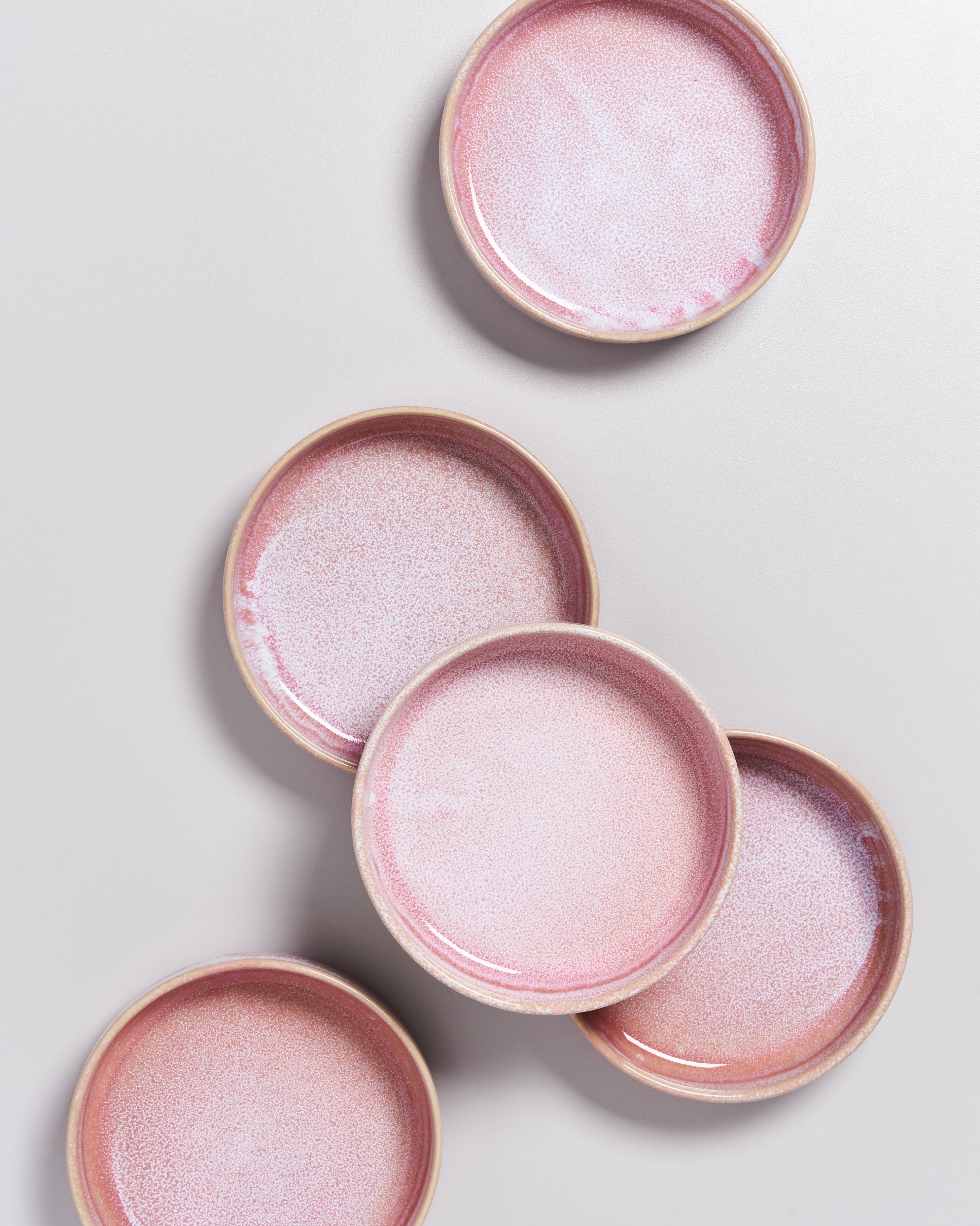 Fünf rosa Keramikteller mit dezentem Muster liegen überlappend auf einer hellgrauen Oberfläche.