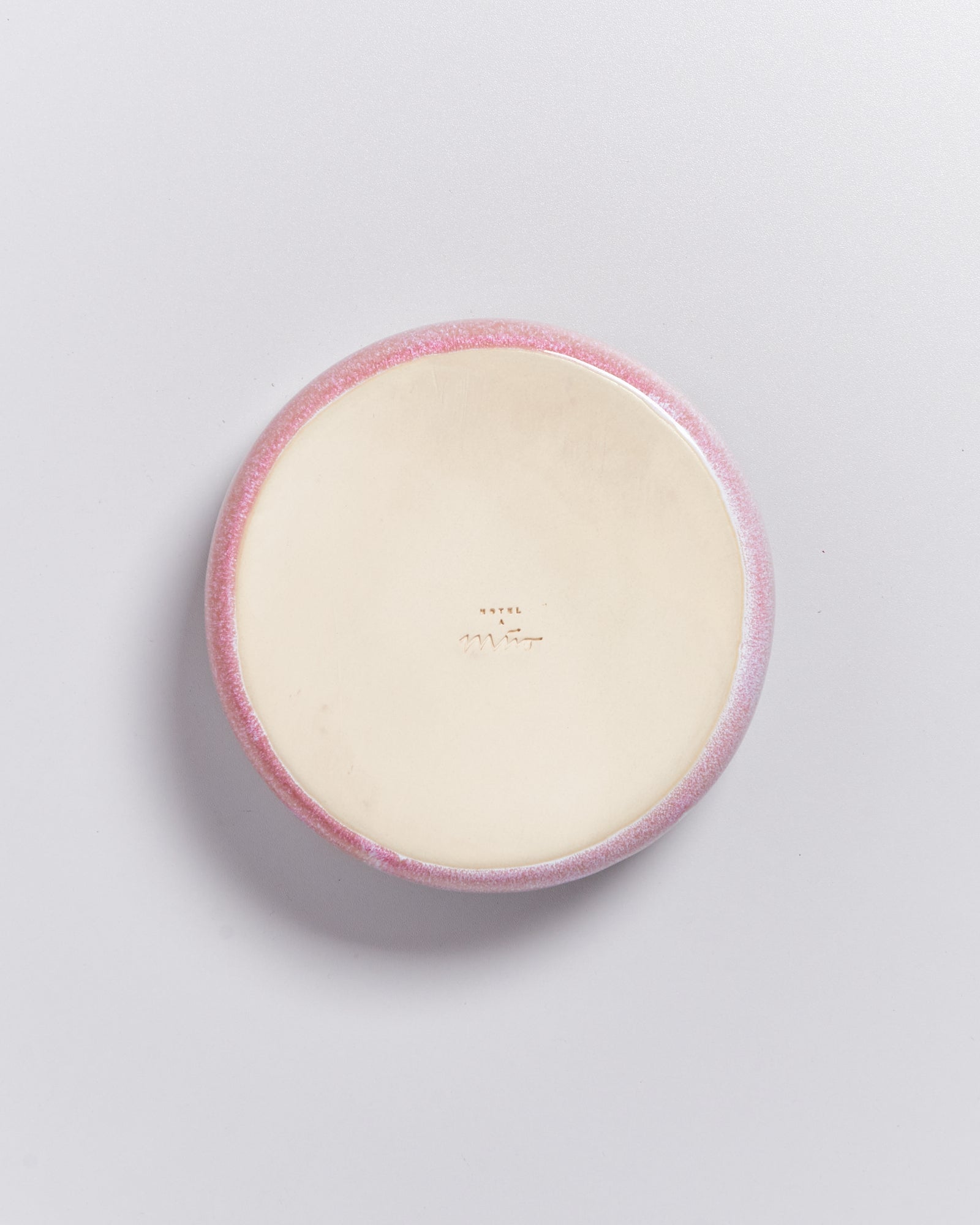 Runde Keramikscheibe mit rosa Rand und unleserlichen Schriftzeichen in der Mitte auf hellem Hintergrund.