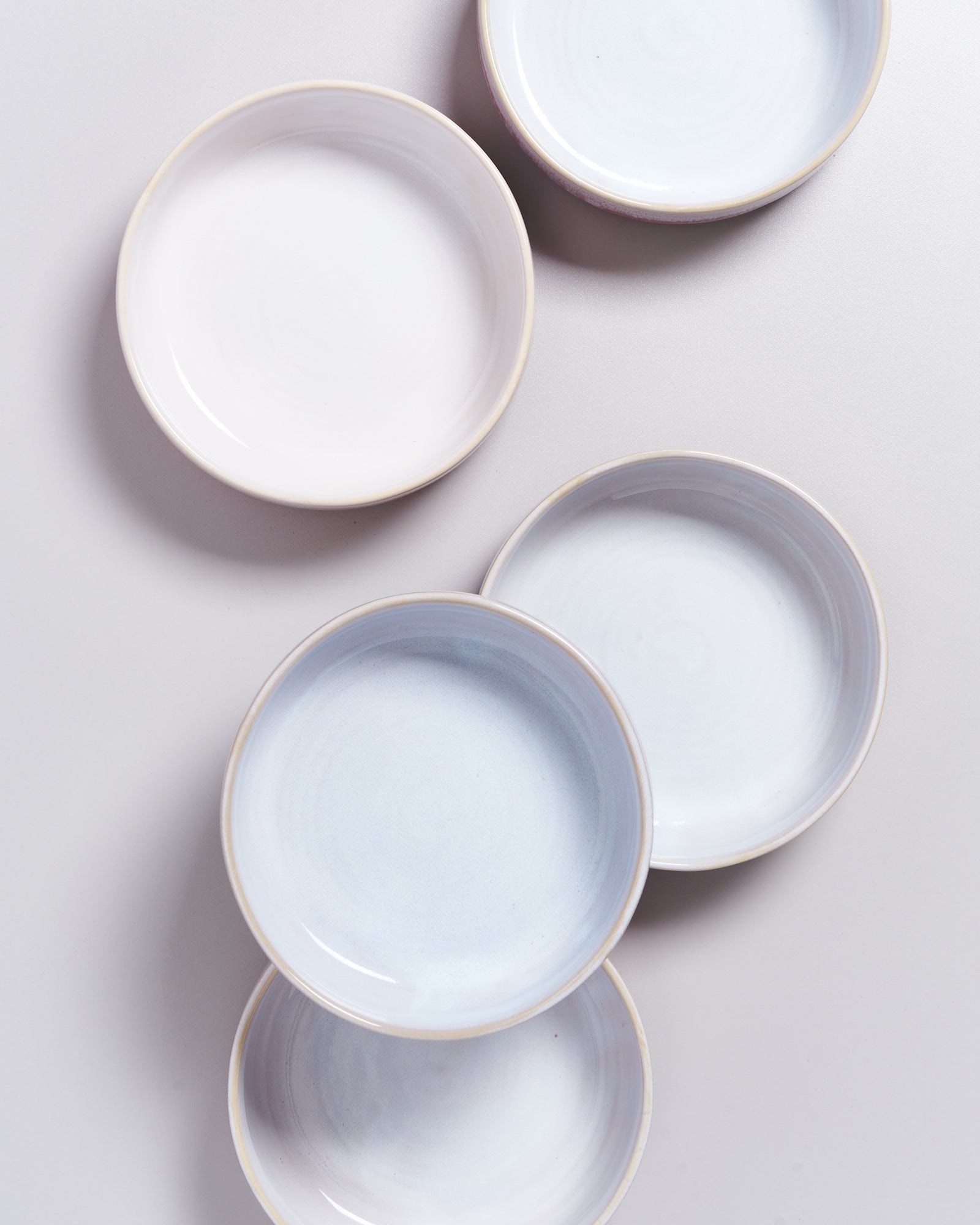 Fünf weiße, runde Keramikteller auf einem hellen Hintergrund, im Muster angeordnet.