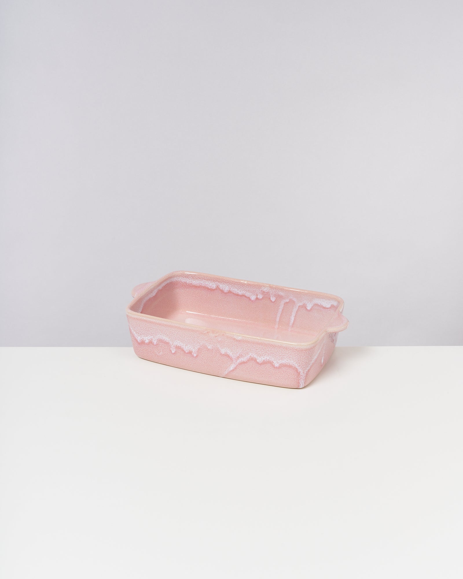 Rosa Backform mit weißen Rändern, die wie zerlaufene Glasur aussehen, auf einem weißen Tisch vor grauem Hintergrund.