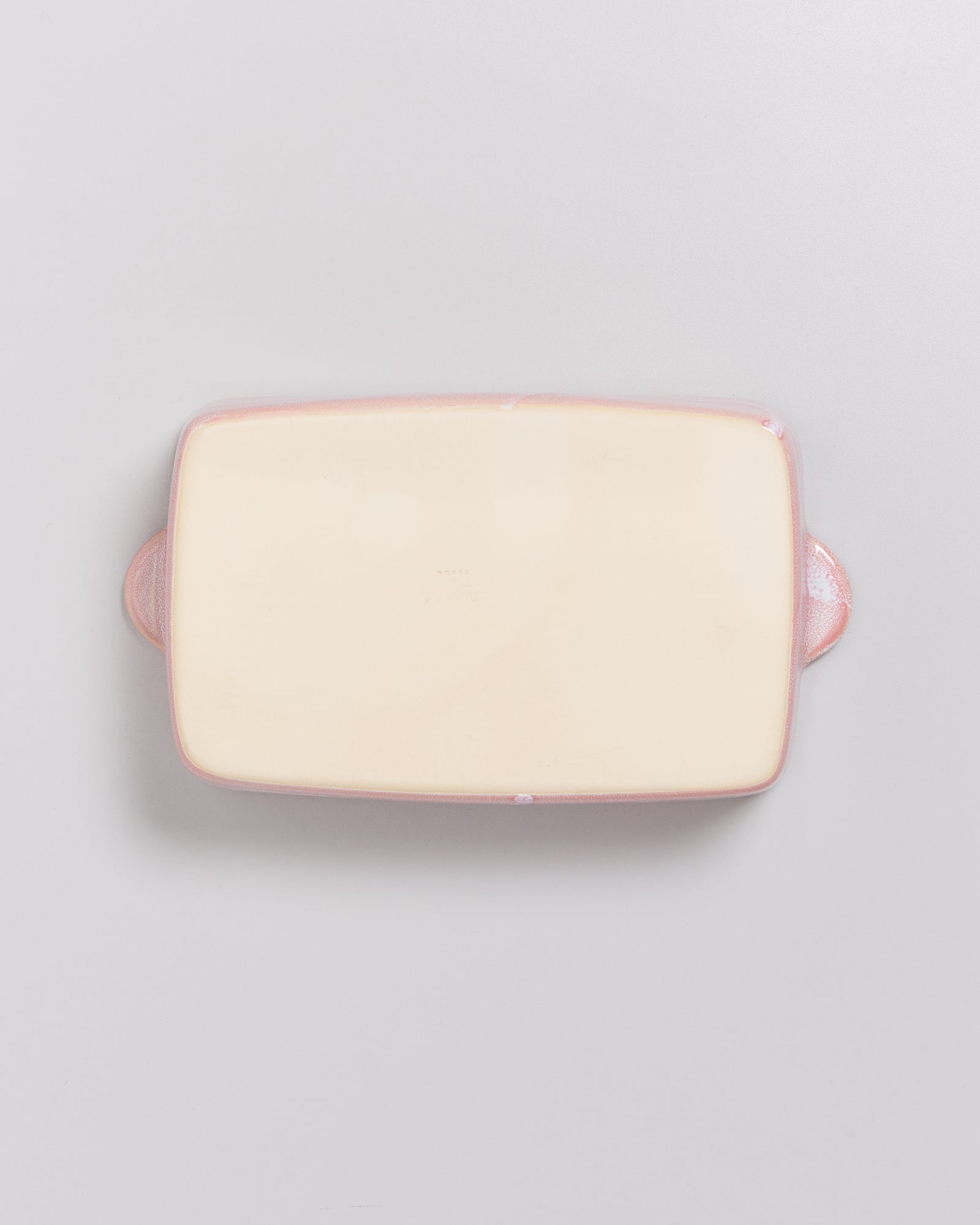 Rechteckige, flache Keramik-Backform mit rosa Griffen auf weißem Hintergrund.