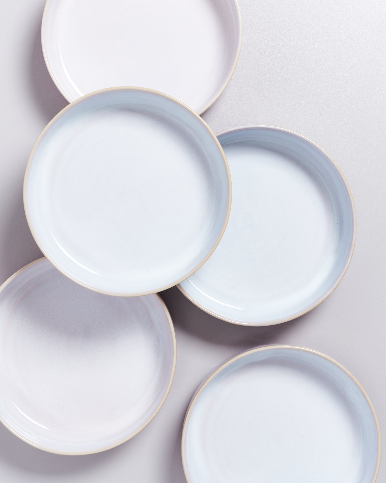 Fünf stapelbare, pastellfarbene Teller mit leichtem Blauton auf einer hellen Oberfläche.
