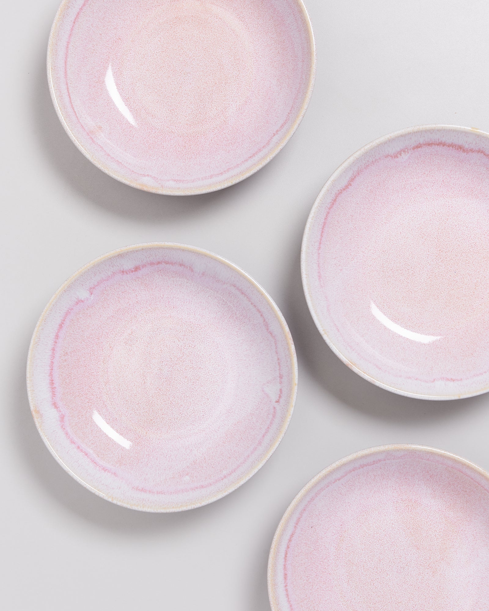 Vier rosa Keramikteller mit einem dezenten Muster auf einem weißen Hintergrund.