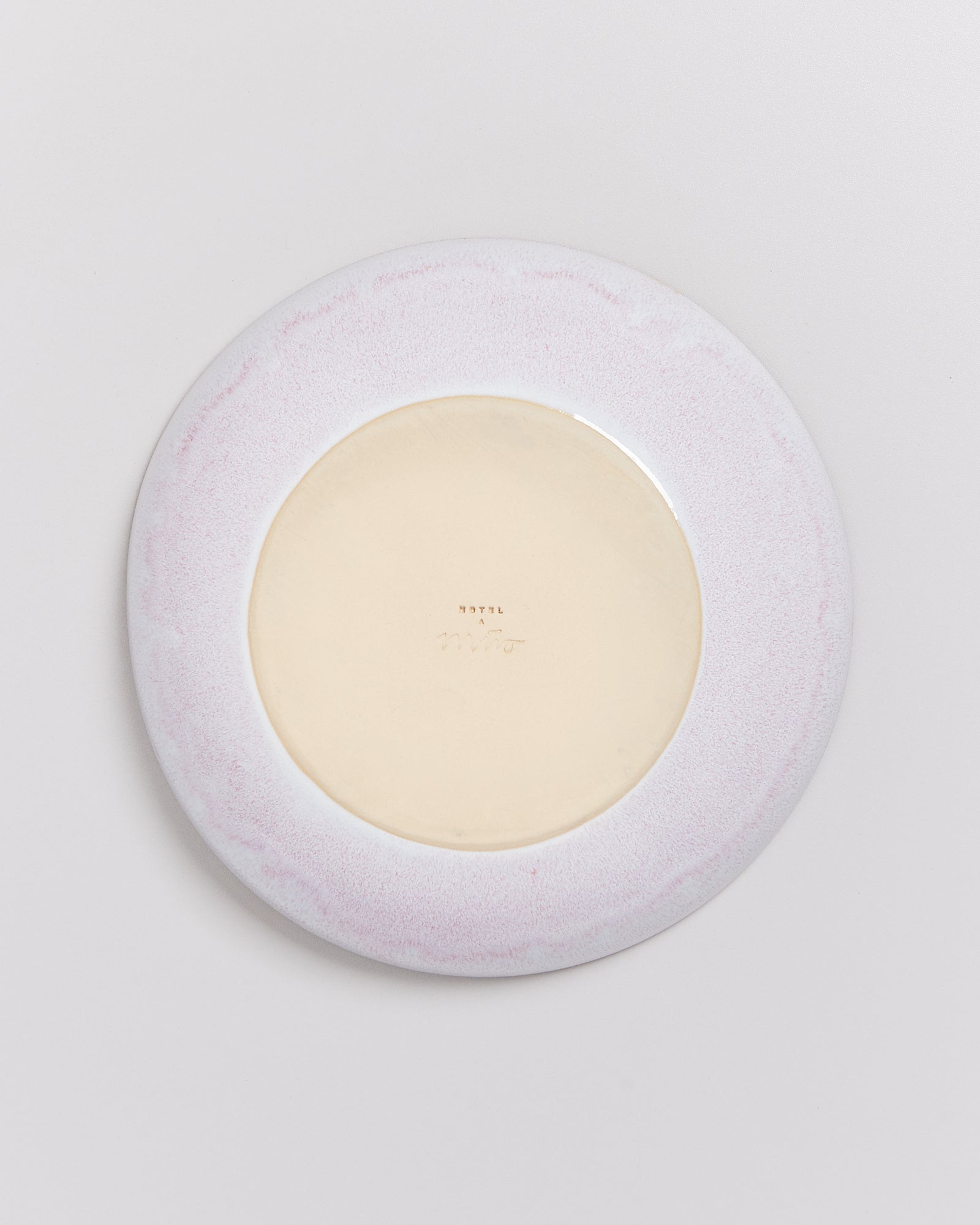 Rückseite eines runden Keramiktellers mit blassem Rosa und beigem Mittelteil auf hellem Hintergrund.