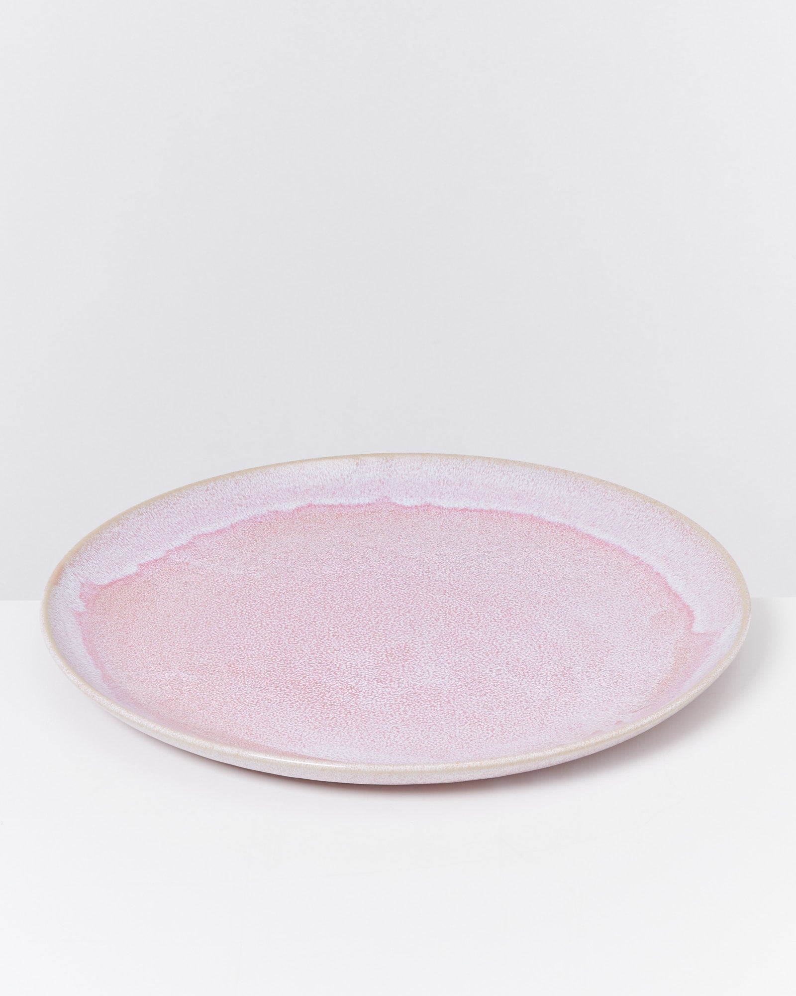 Runder, flacher Teller mit rosa und beigefarbener Glasur auf einem weißen Hintergrund.
