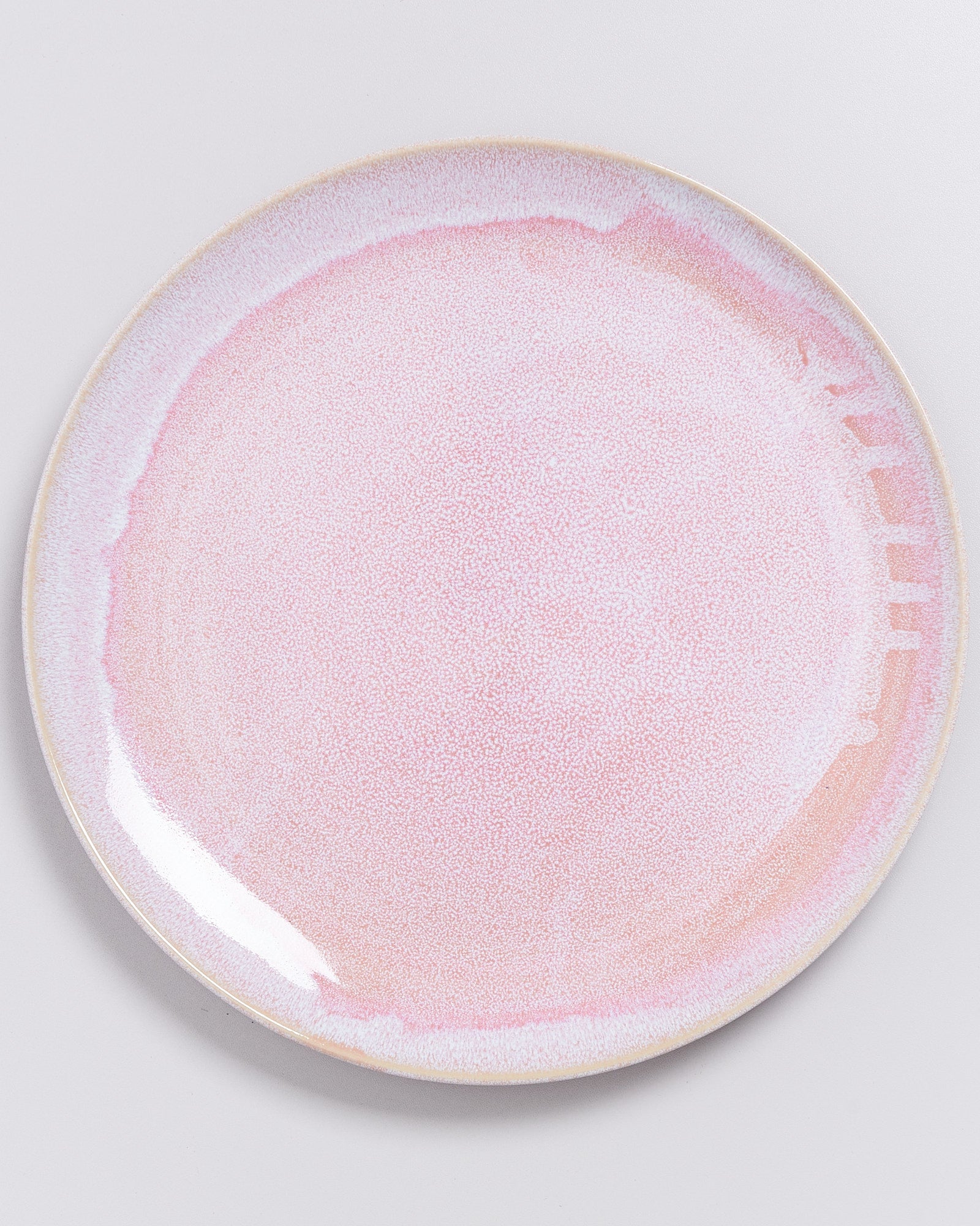 Runder Teller mit einer rosa lasierten Oberfläche auf einem hellgrauen Hintergrund.