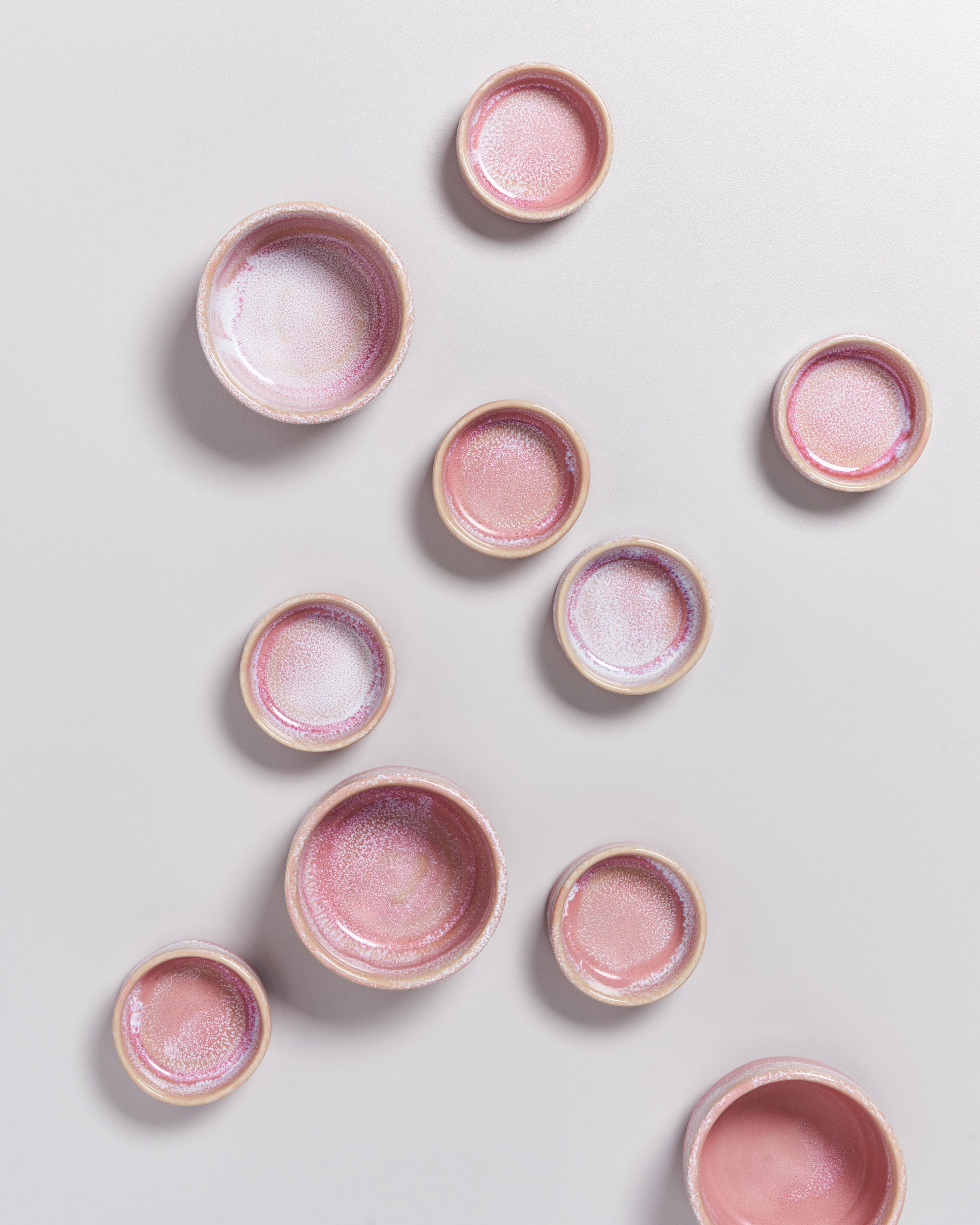 Mehrere kleine, rosa Keramikschalen mit glänzender Glasur auf hellem Hintergrund verstreut.