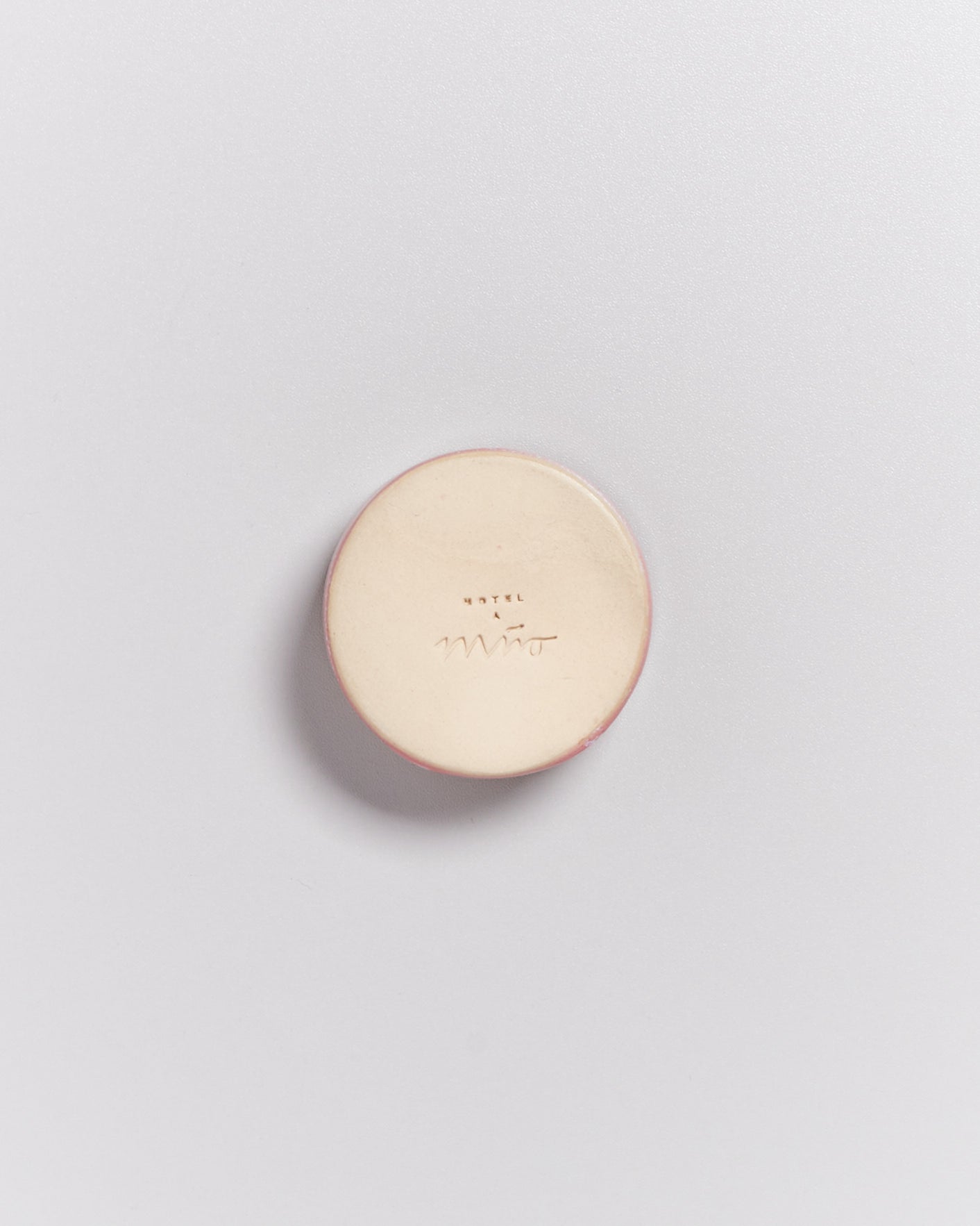 Eine runde, elfenbeinfarbene Seife mit der Aufschrift "Hotel Miró" auf einer hellen Oberfläche.