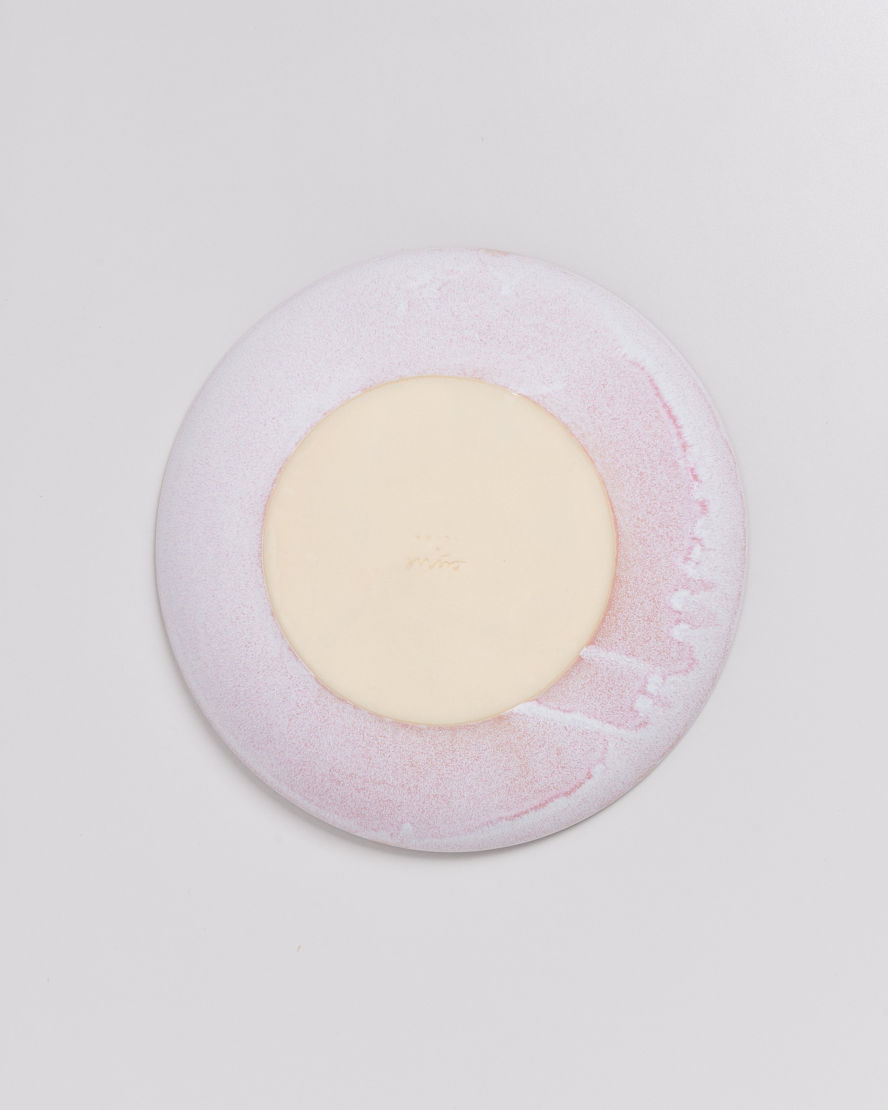 Runder Teller in hellem Rosa und Creme auf weißem Hintergrund.