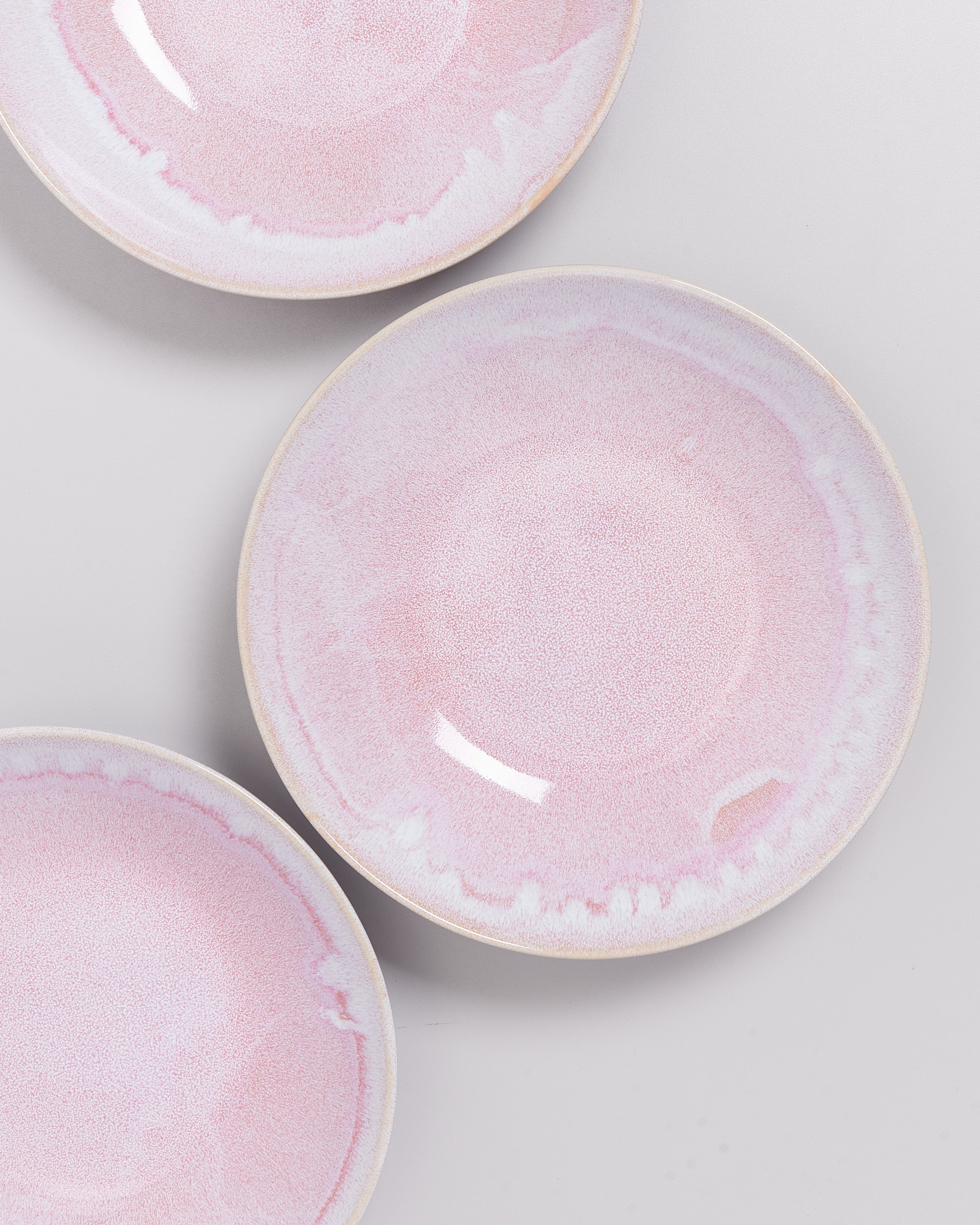 Drei rosa Keramikteller mit hellem Rand auf grauem Hintergrund von oben fotografiert.