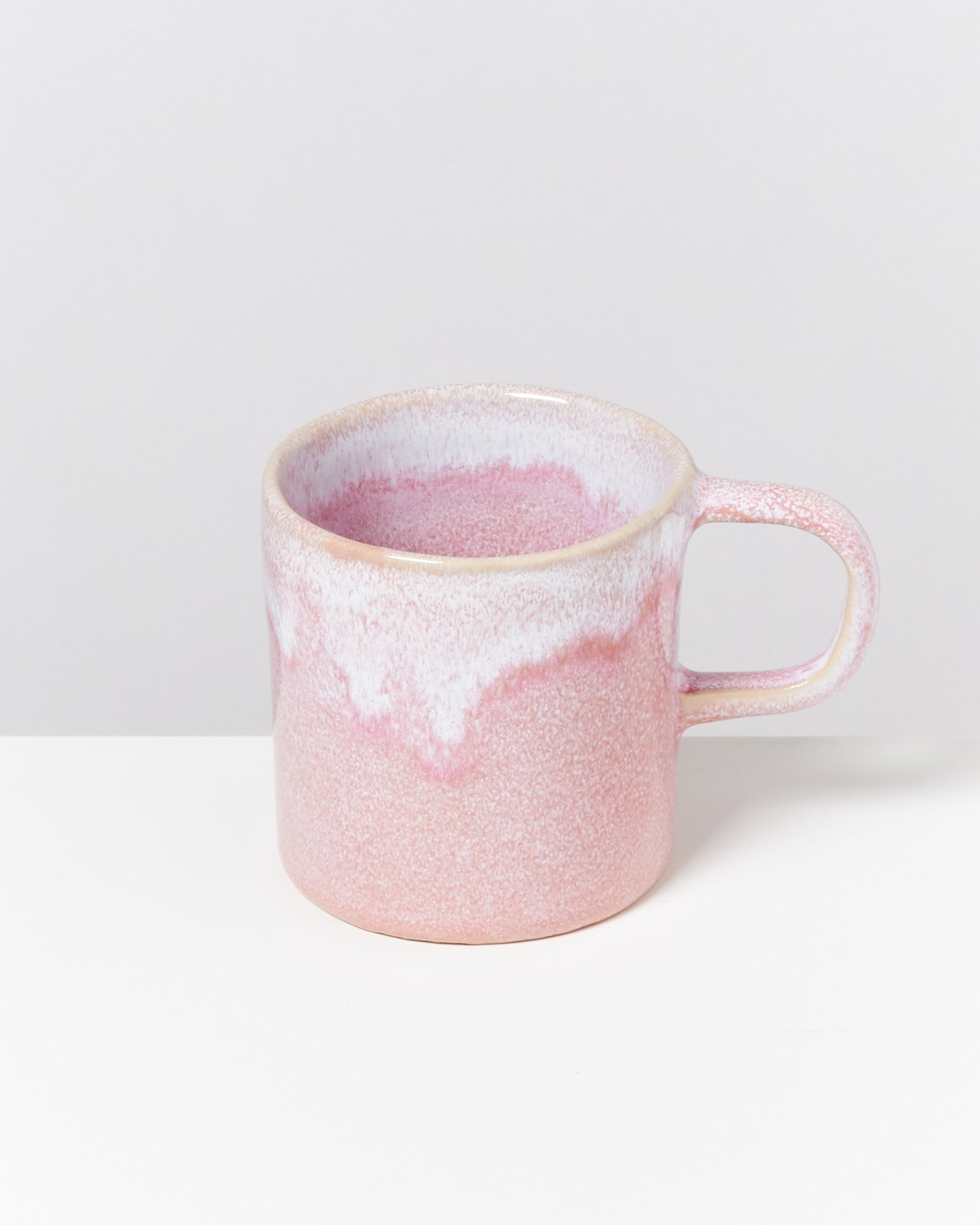 Rosa, keramikbeschichtete Tasse mit Henkel auf einer weißen Oberfläche vor grauem Hintergrund.