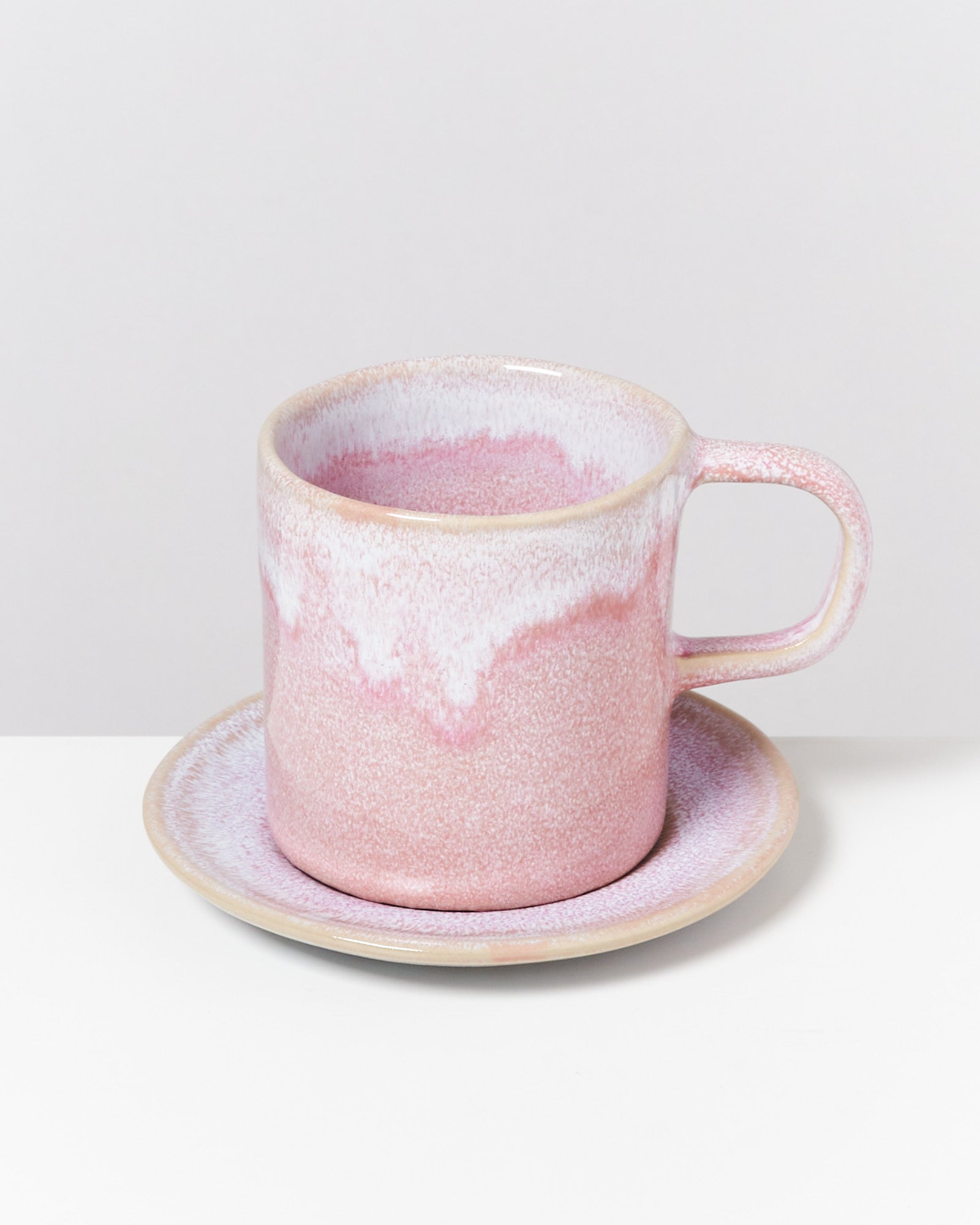 Eine rosafarbene Keramiktasse mit Untertasse auf einem weißen Hintergrund.