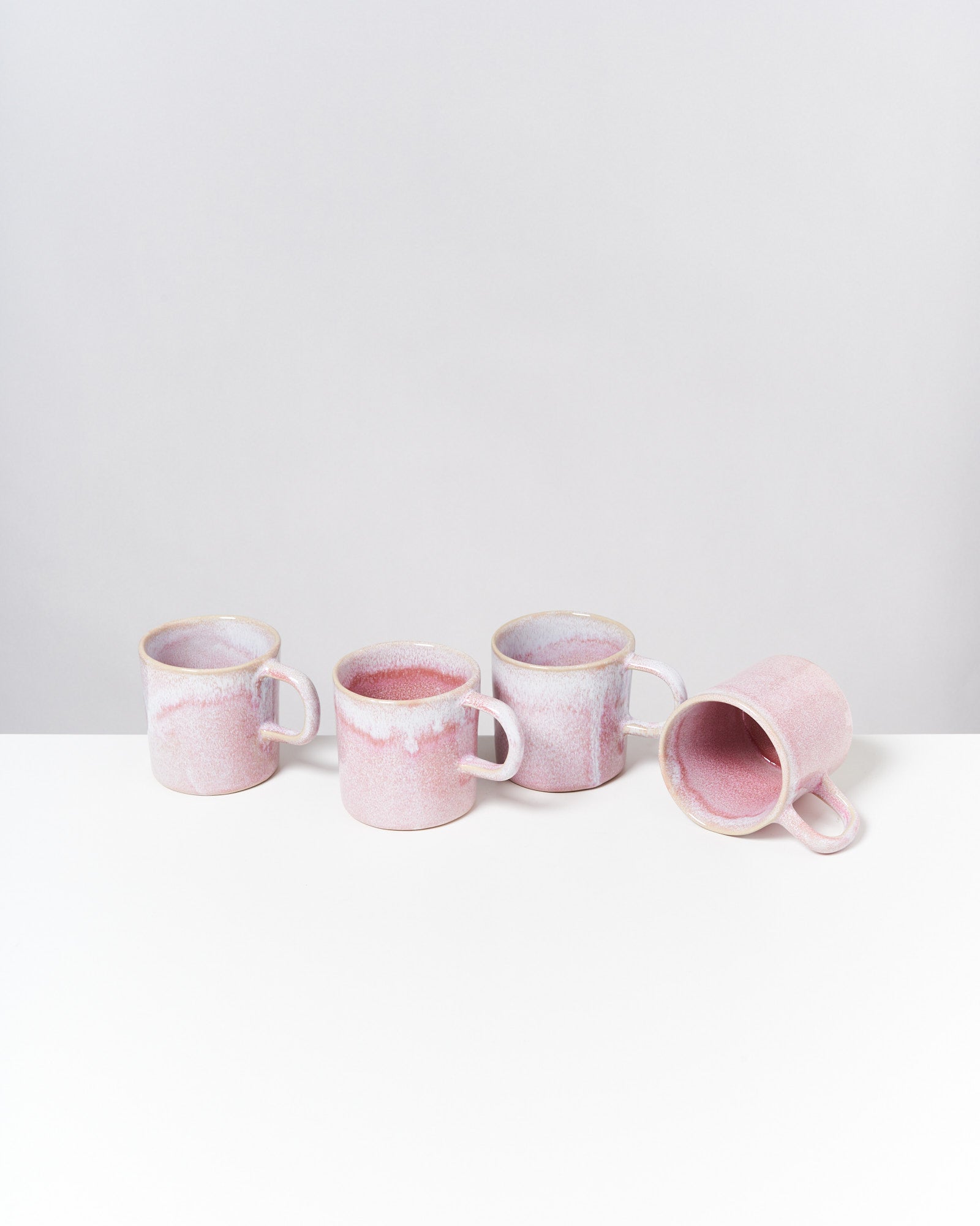 Vier rosa Tassen mit Henkel auf einem weißen Tisch, eine liegt seitlich.