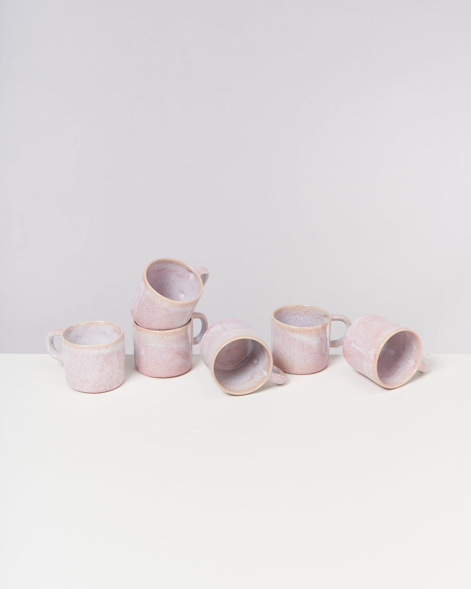 Sechs rosa Keramiktassen auf einer weißen Oberfläche, eine davon liegt auf der Seite.