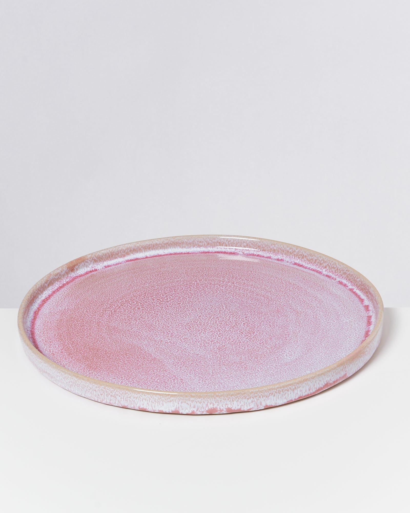 Runder rosa Keramikteller mit glatter Oberfläche auf einem weißen Hintergrund.