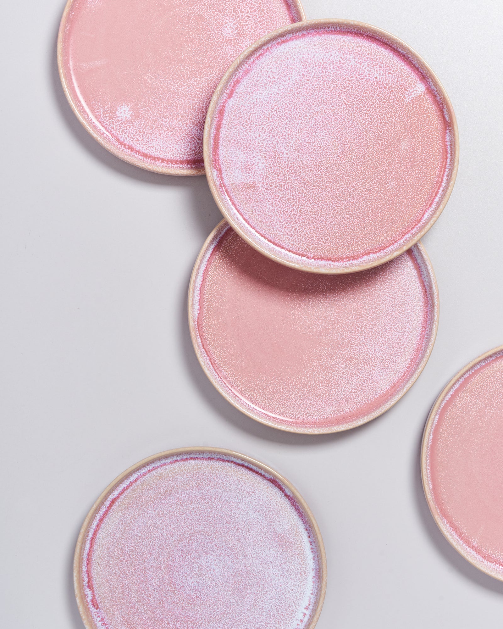 Fünf rosa Keramikteller mit dünnem Rand, auf weißem Hintergrund angeordnet.