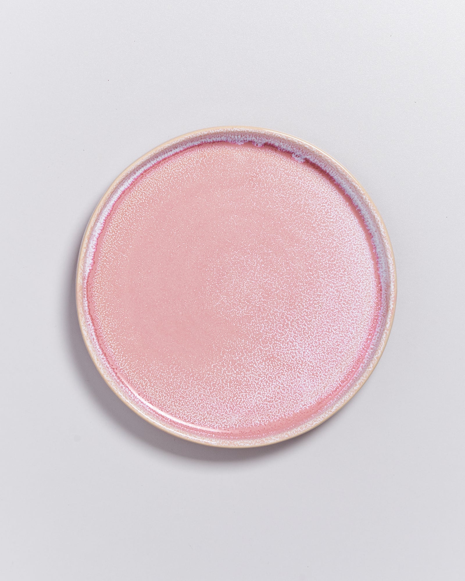 Rosa, runde Keramikplatte auf hellgrauem Hintergrund.