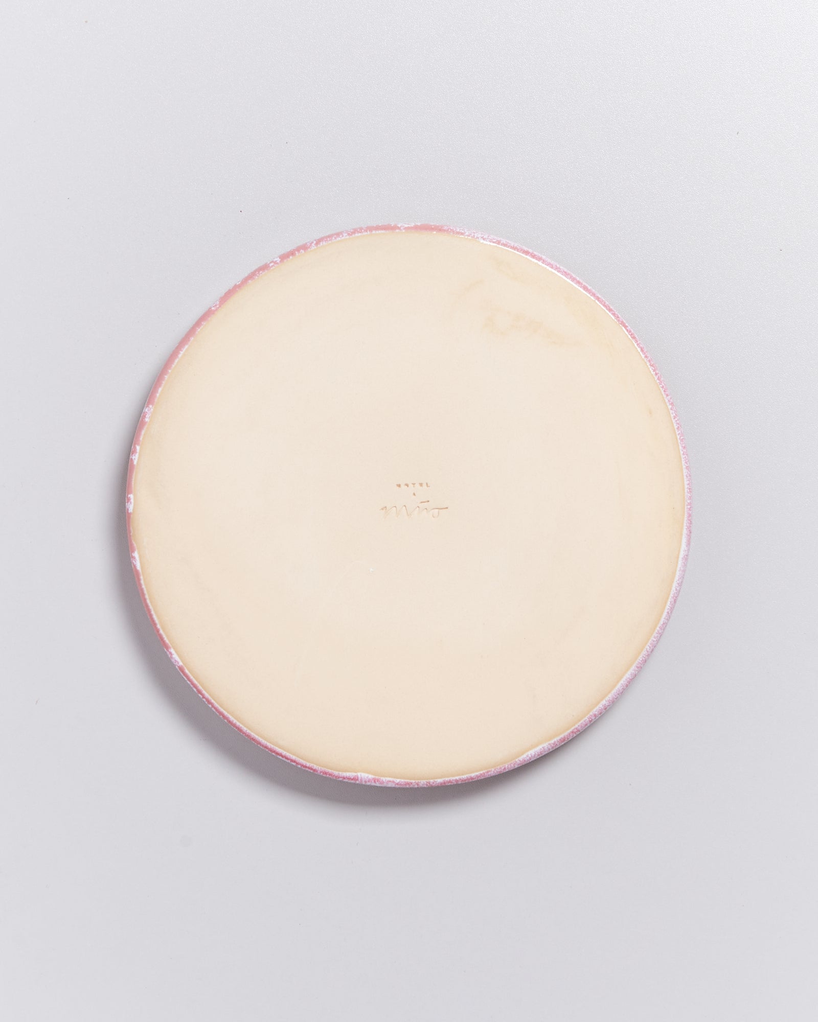 Runde, pastellfarbene Keramikplatte mit dezenter Prägung auf der Unterseite, auf hellem Hintergrund.