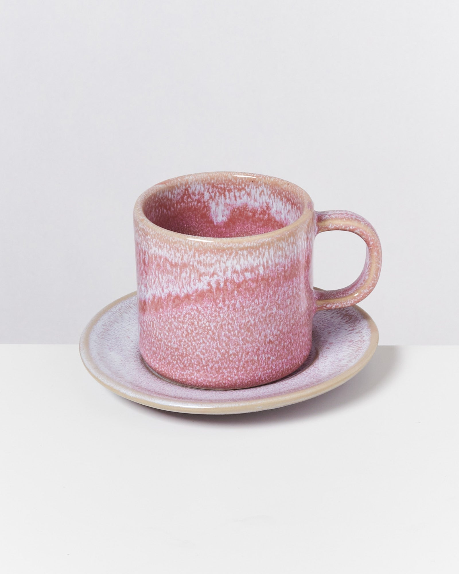 Rosa Keramik-Tasse und Untertasse auf weißem Hintergrund.