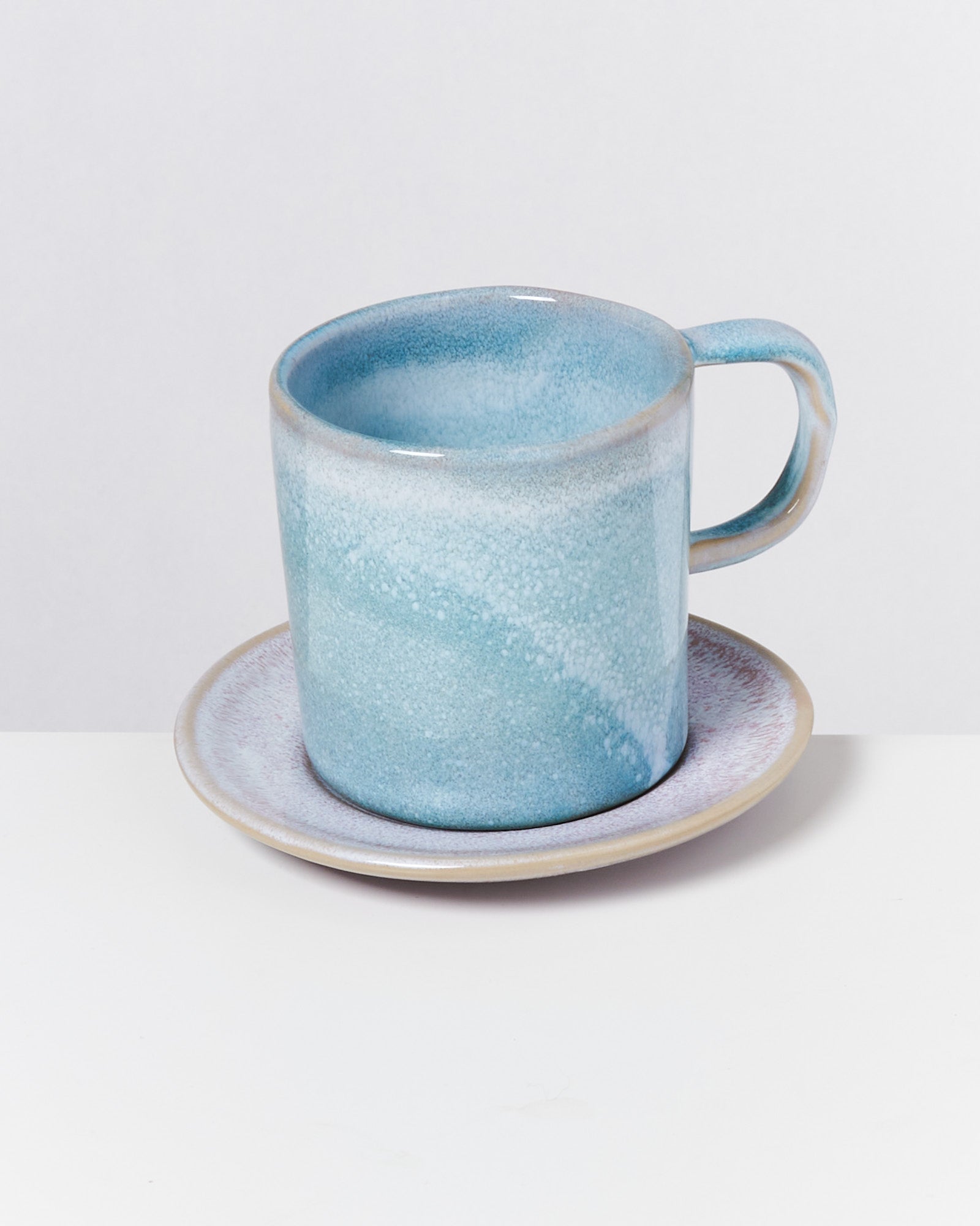 Blaue Keramiktasse mit Unterteller vor hellem Hintergrund.