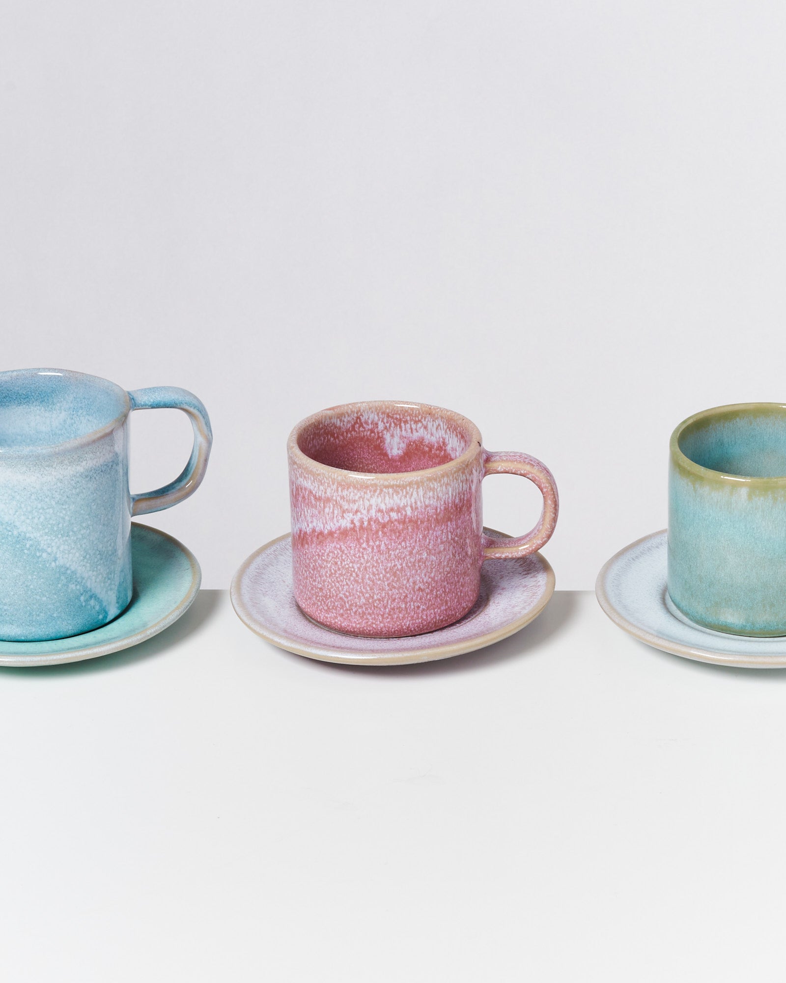 Drei bunte Keramik-Tassen mit passenden Untertassen auf einem weißen Hintergrund.